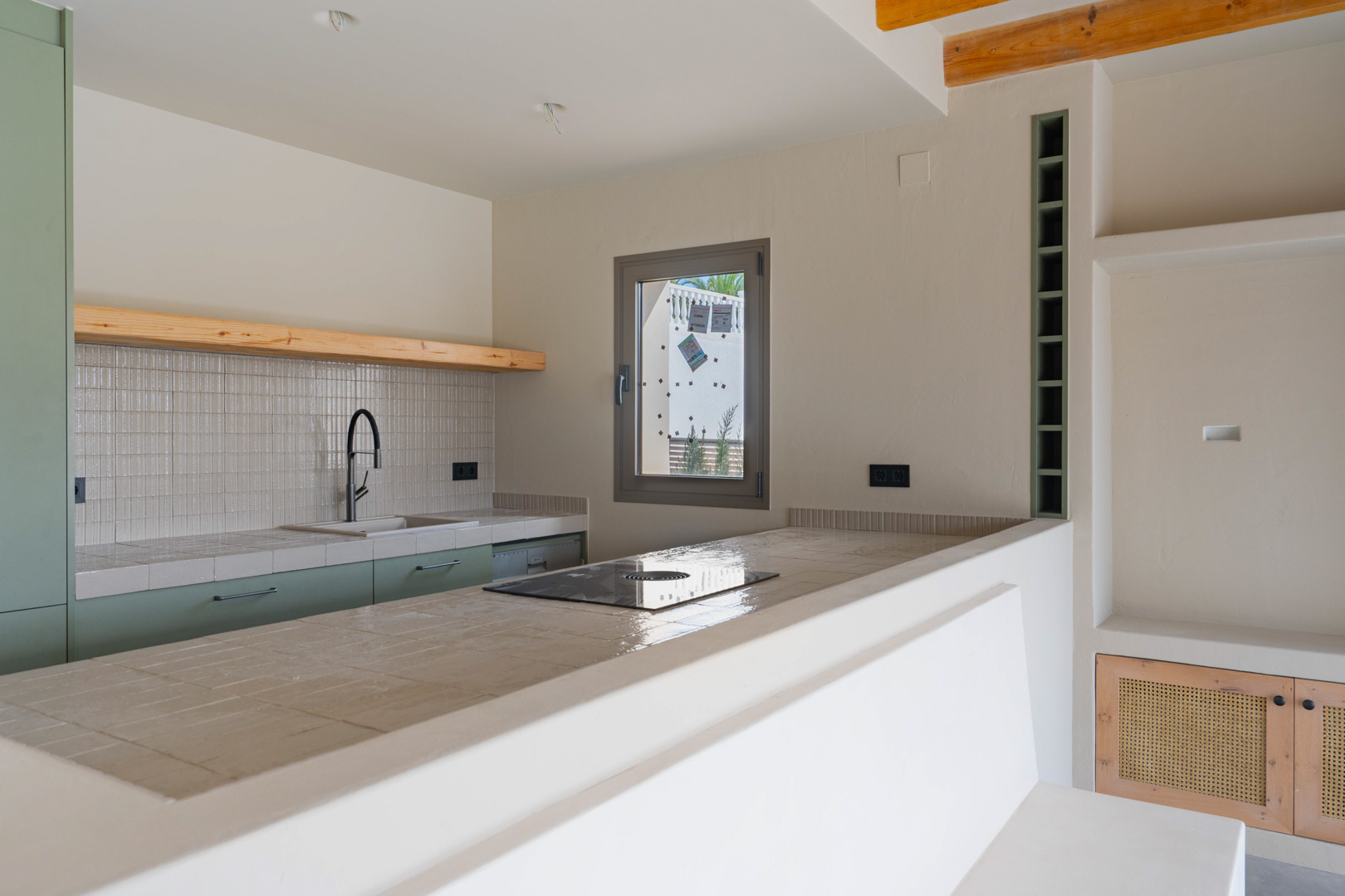 Designer kitchen featuring porcelain countertops, integrated induction hob, and sage green cabinetry. Clay-finish walls and natural wood accents create a warm, organic atmosphere.