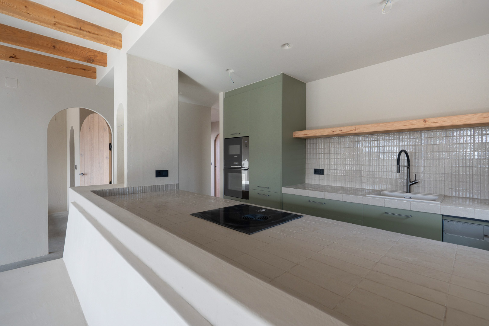 Designer kitchen with sage green cabinetry, Ragno porcelain countertops, and a Bora induction hob. Features exposed wooden beams and natural clay wall finishes.