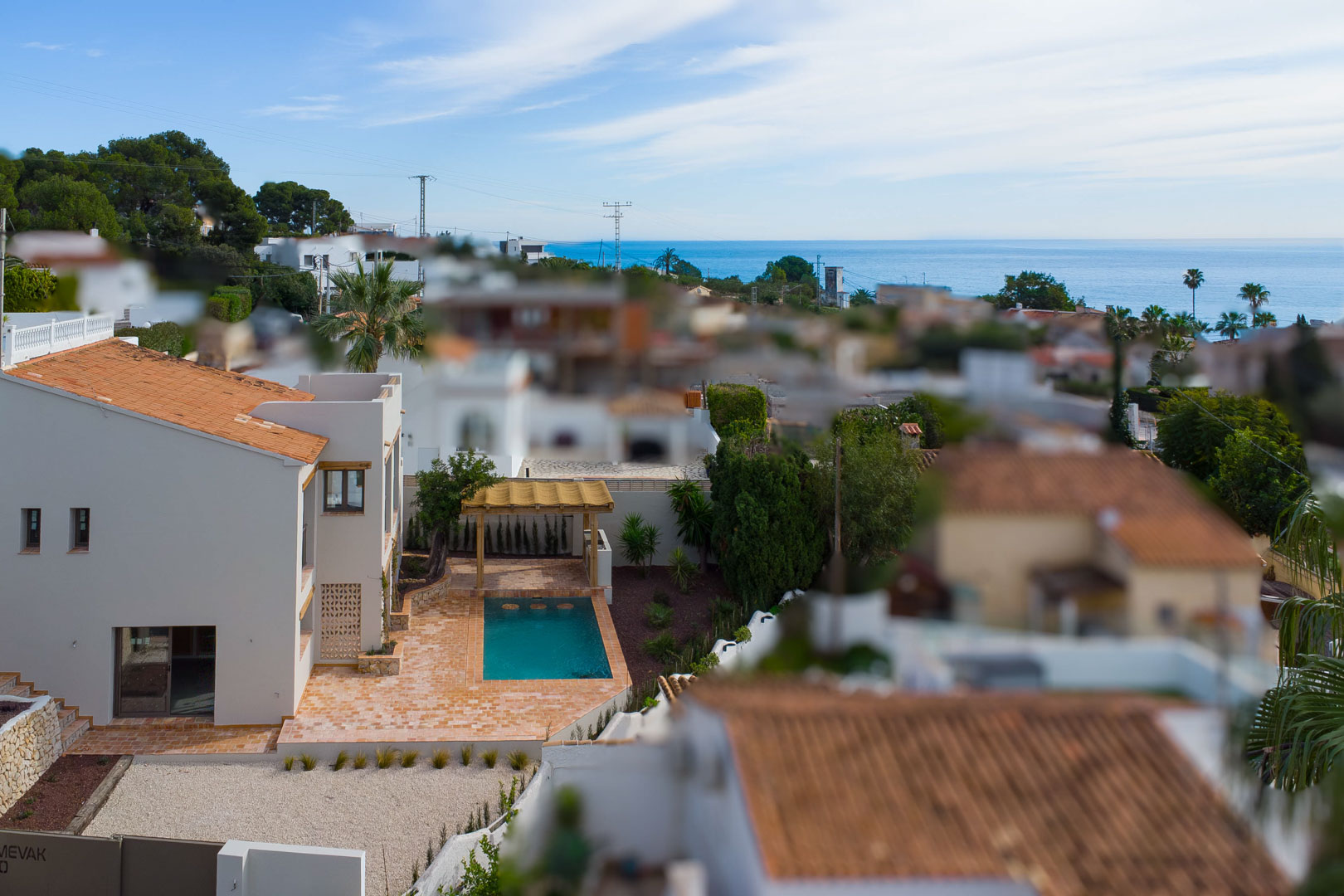 Elevated view of the villa featuring the private pool, terracotta terrace, and wooden pergola, with the Mediterranean Sea visible on the horizon.