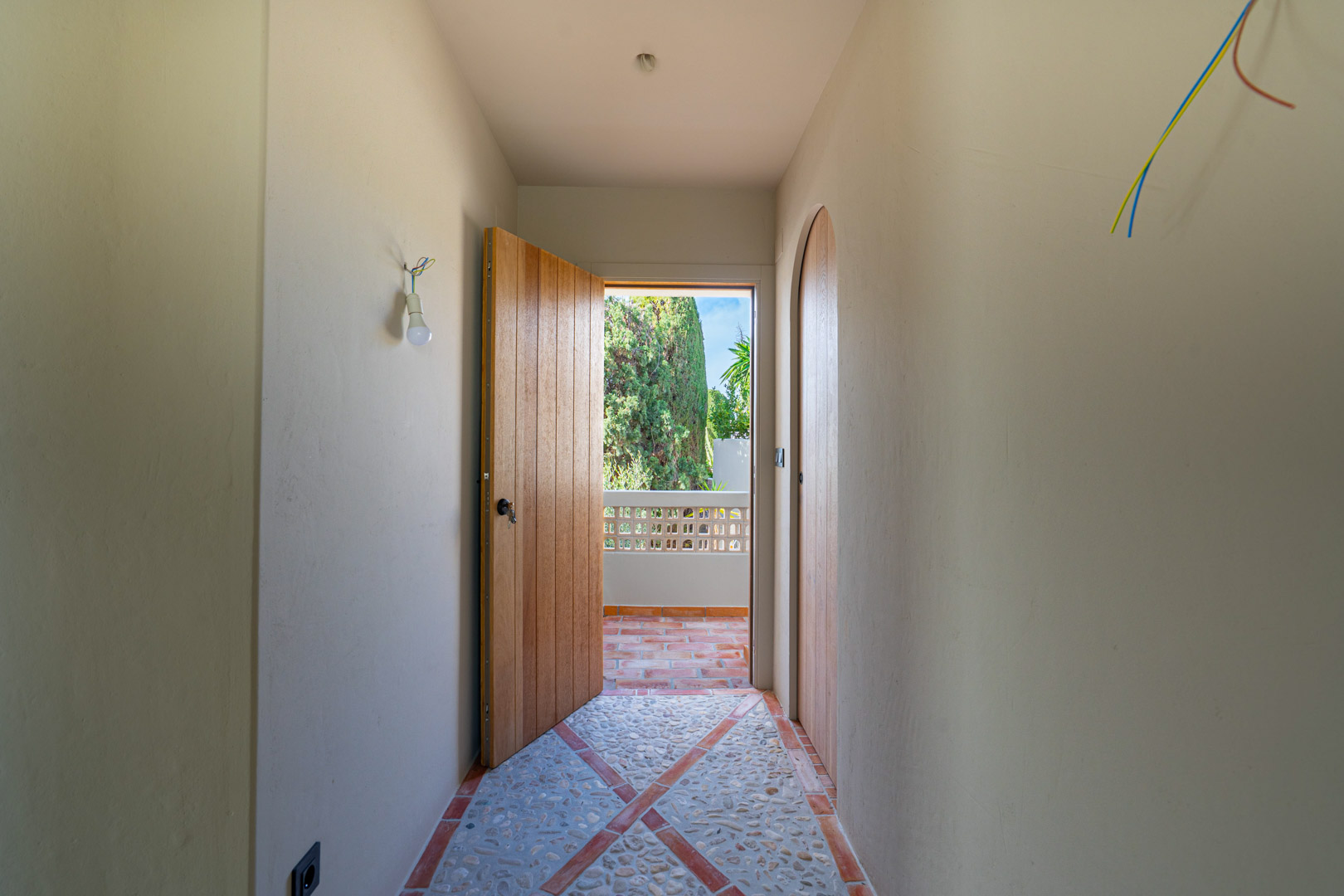 Hallway featuring patterned pebble and terracotta flooring, clay-finished walls, and solid oak doors opening onto a terrace with garden views.