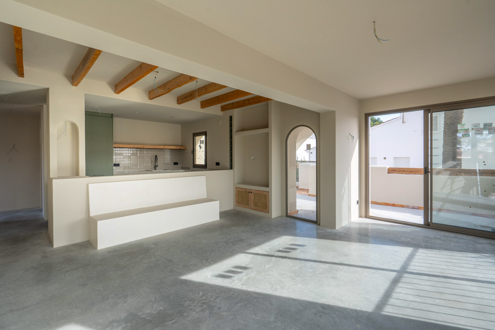 Open-plan living area featuring polished concrete floors, exposed wooden ceiling beams, and a minimalist built-in bench with access to the terrace.