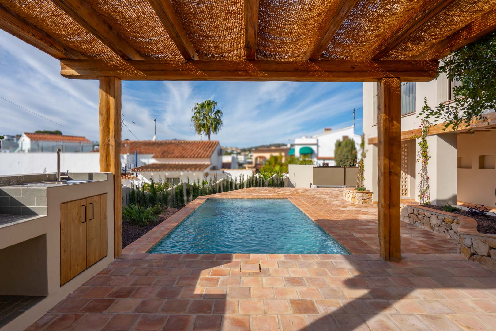 Outdoor terrace featuring terracotta tiling, a wooden pergola with natural shading, and a built-in BBQ area adjacent to the new swimming pool.