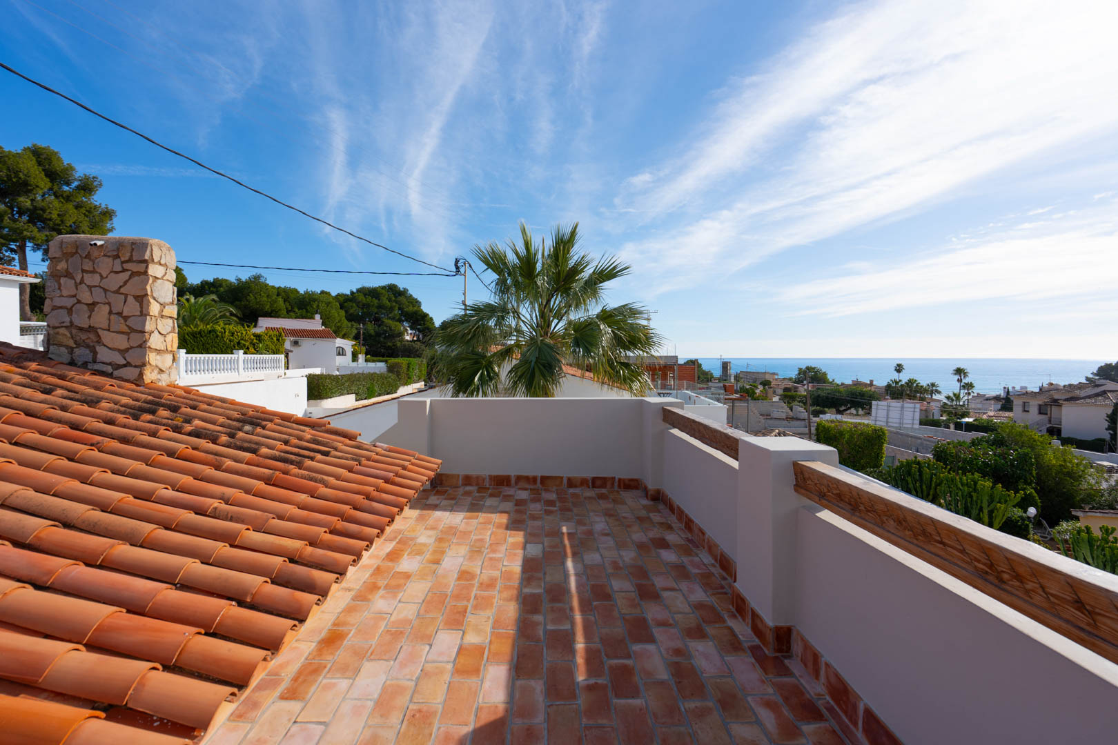 Rooftop terrace featuring terracotta flooring and panoramic Mediterranean Sea views. Includes a natural stone chimney and traditional clay roof tiles under a clear sky.