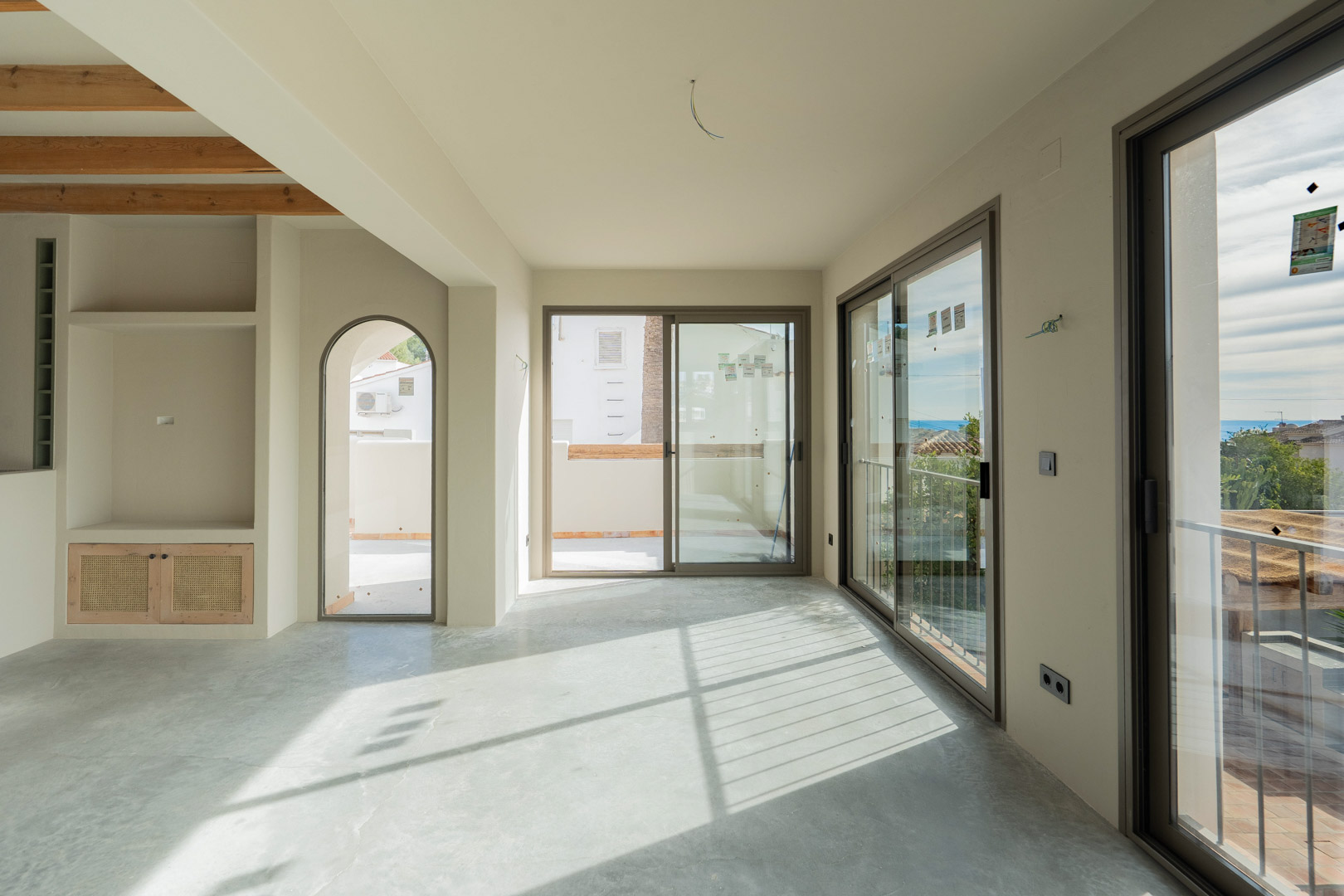 Spacious living area with polished concrete floors, integrated shelving, and large sliding glass doors providing natural light and Mediterranean sea views.
