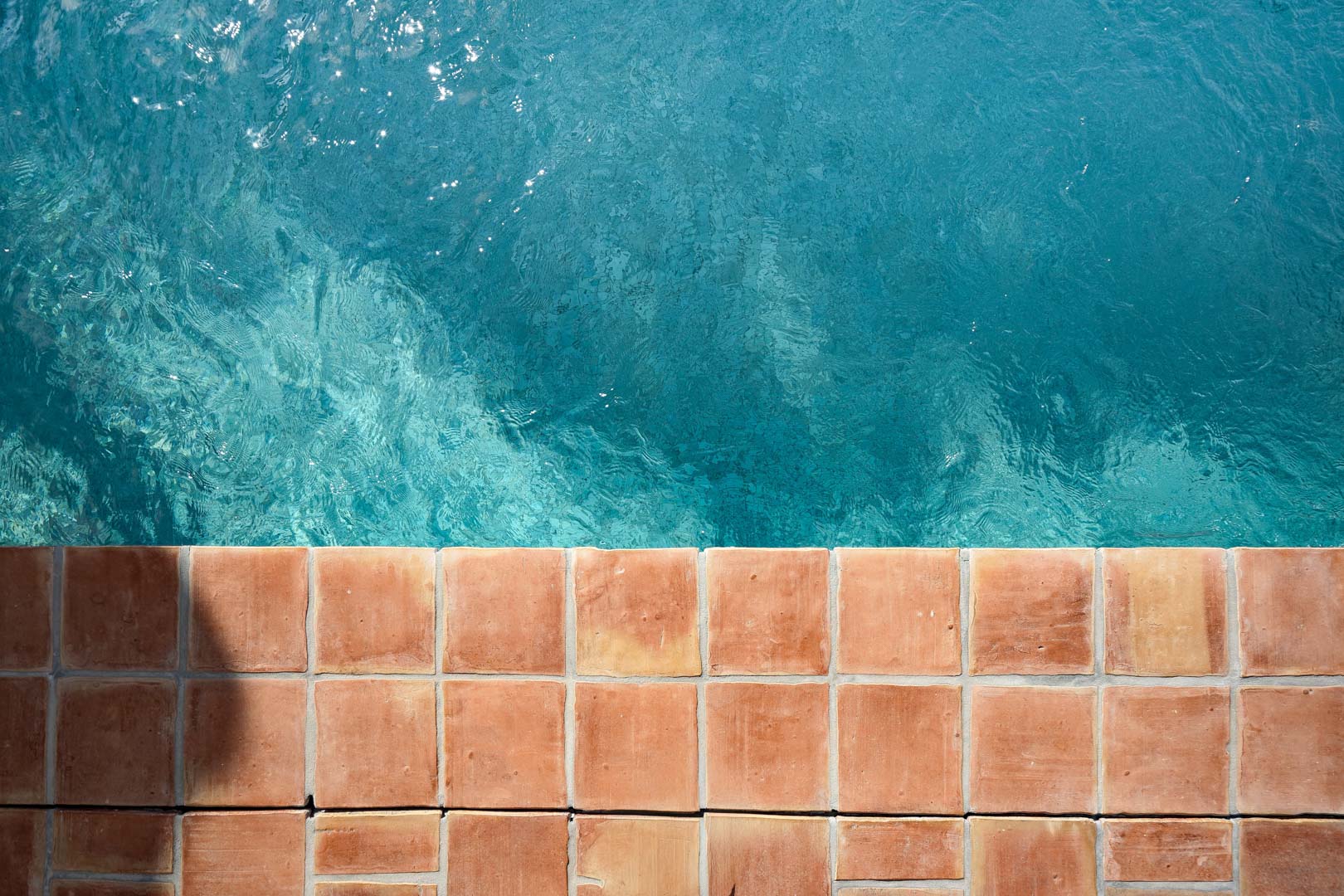 Top-down view of the swimming pool edge featuring natural terracotta tiles and clear turquoise water, showcasing the property's Mediterranean aesthetic.