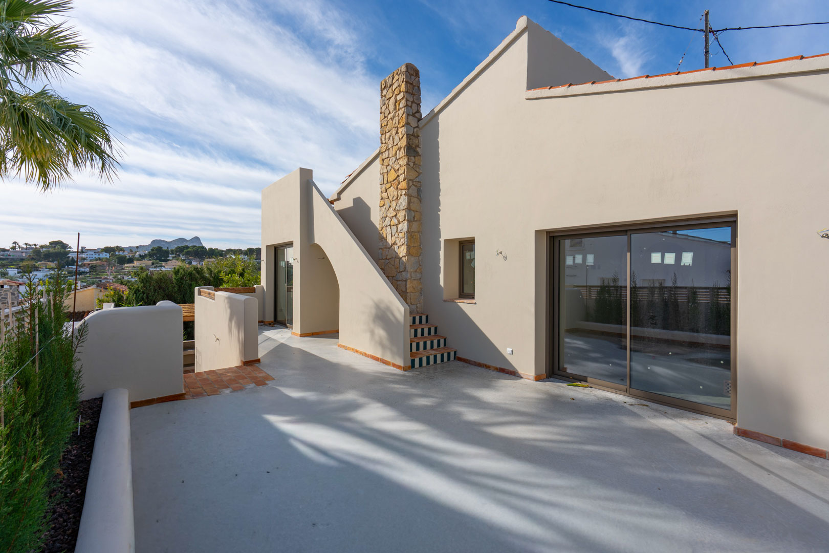 Upper terrace featuring polished concrete flooring, a natural stone chimney, and distant views of the Peñón de Ifach rock formation.
