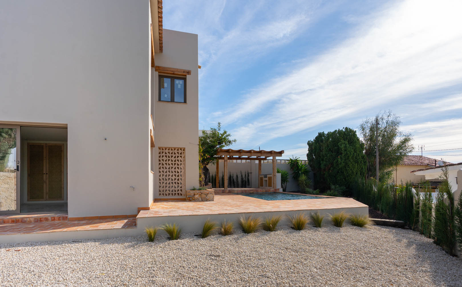 Villa exterior featuring a terracotta tile terrace, newly built swimming pool, and wooden pergola over the BBQ area, set within a low-maintenance gravel garden.