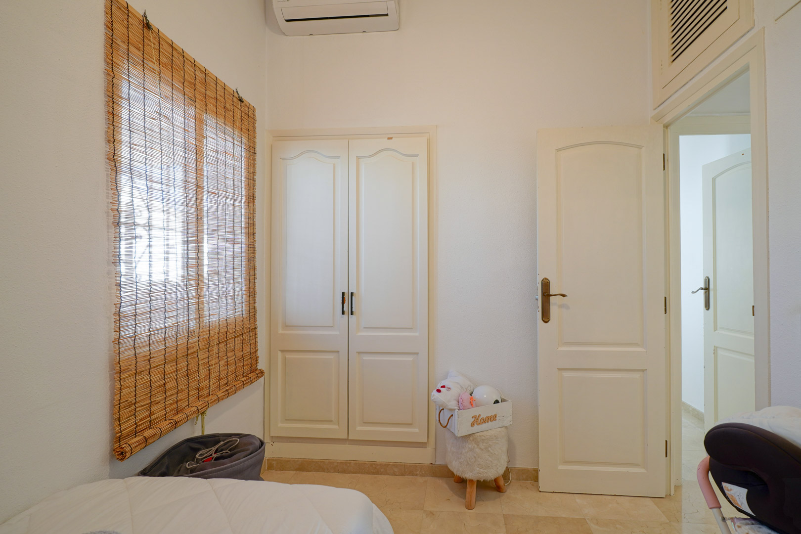 Bright bedroom featuring a white built-in wardrobe, split-system air conditioning, and a window with a natural bamboo blind.
