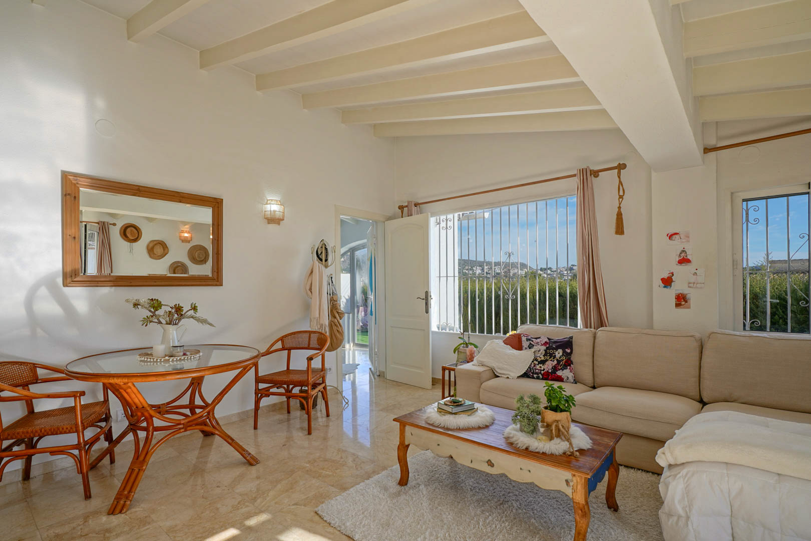 Bright living and dining area featuring exposed ceiling beams, polished marble floors, and a large window providing natural light and open landscape views.