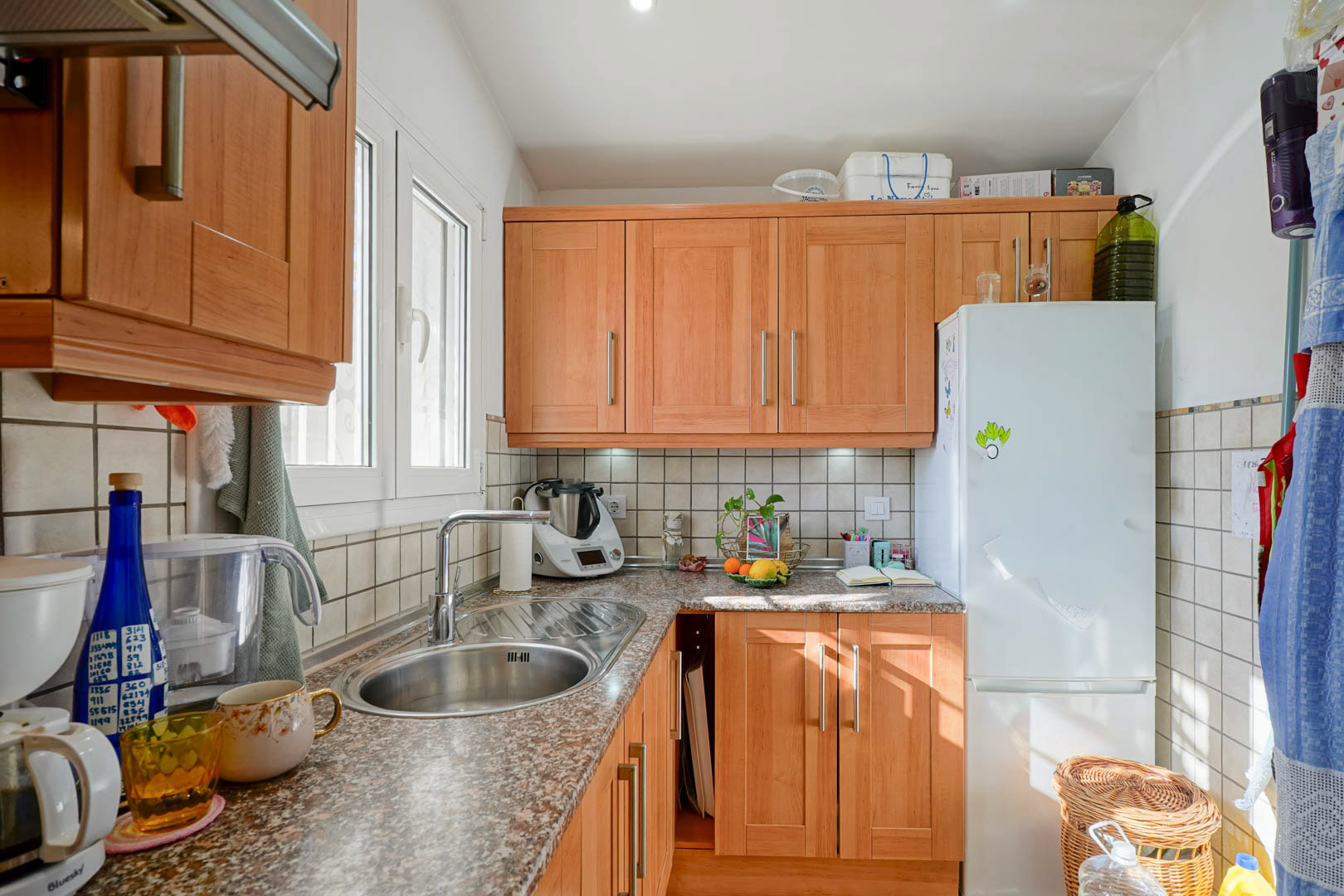 Independent kitchen featuring wooden cabinetry, granite countertops, and a stainless steel sink. Natural light enters through a side window, highlighting the functional layout.