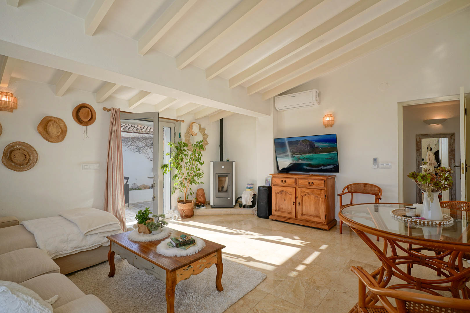Living-dining area featuring white exposed wooden beams, a pellet stove, and marble flooring. The room includes air conditioning and direct access to the sunlit terrace.