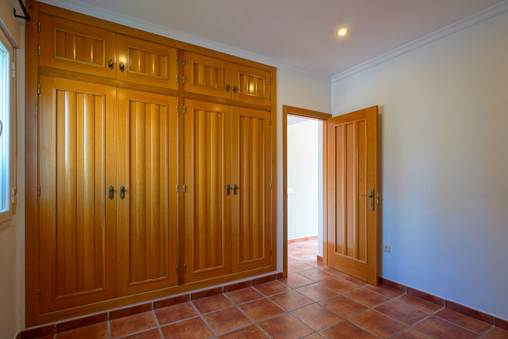 Bedroom featuring a large floor-to-ceiling built-in wooden wardrobe, traditional terracotta tile flooring, and recessed ceiling lighting.