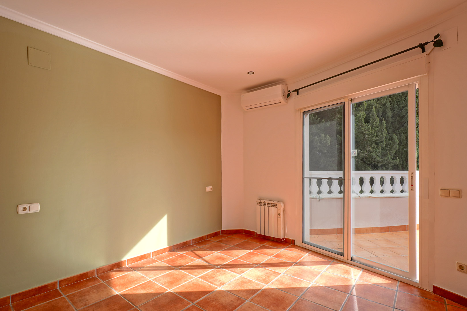 Bright room with a green accent wall, terracotta tiles, and terrace access. Features include split air conditioning, an electric radiator, and natural light.