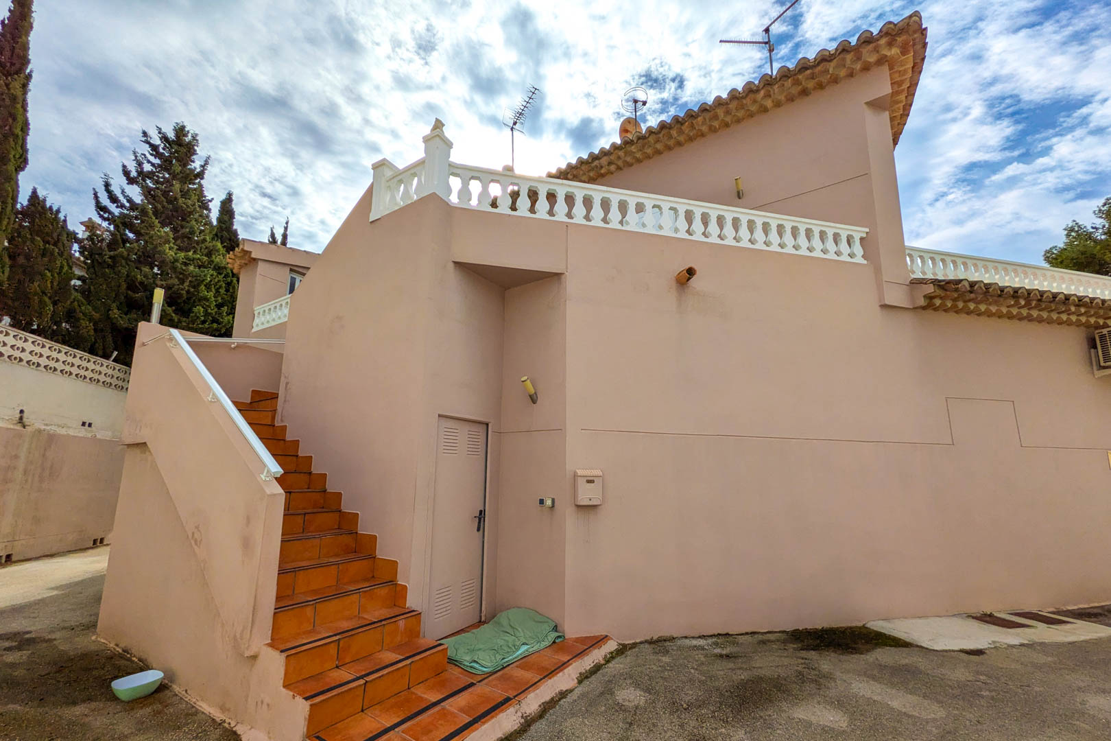Exterior terracotta-tiled staircase leading to the upper floor, featuring a salmon-colored facade and a terrace with a classic white balustrade.