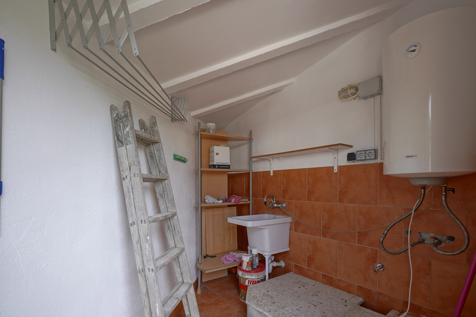 Functional laundry and storage room featuring sloped ceilings, an electric water heater, utility sink, and wall-mounted drying rack.