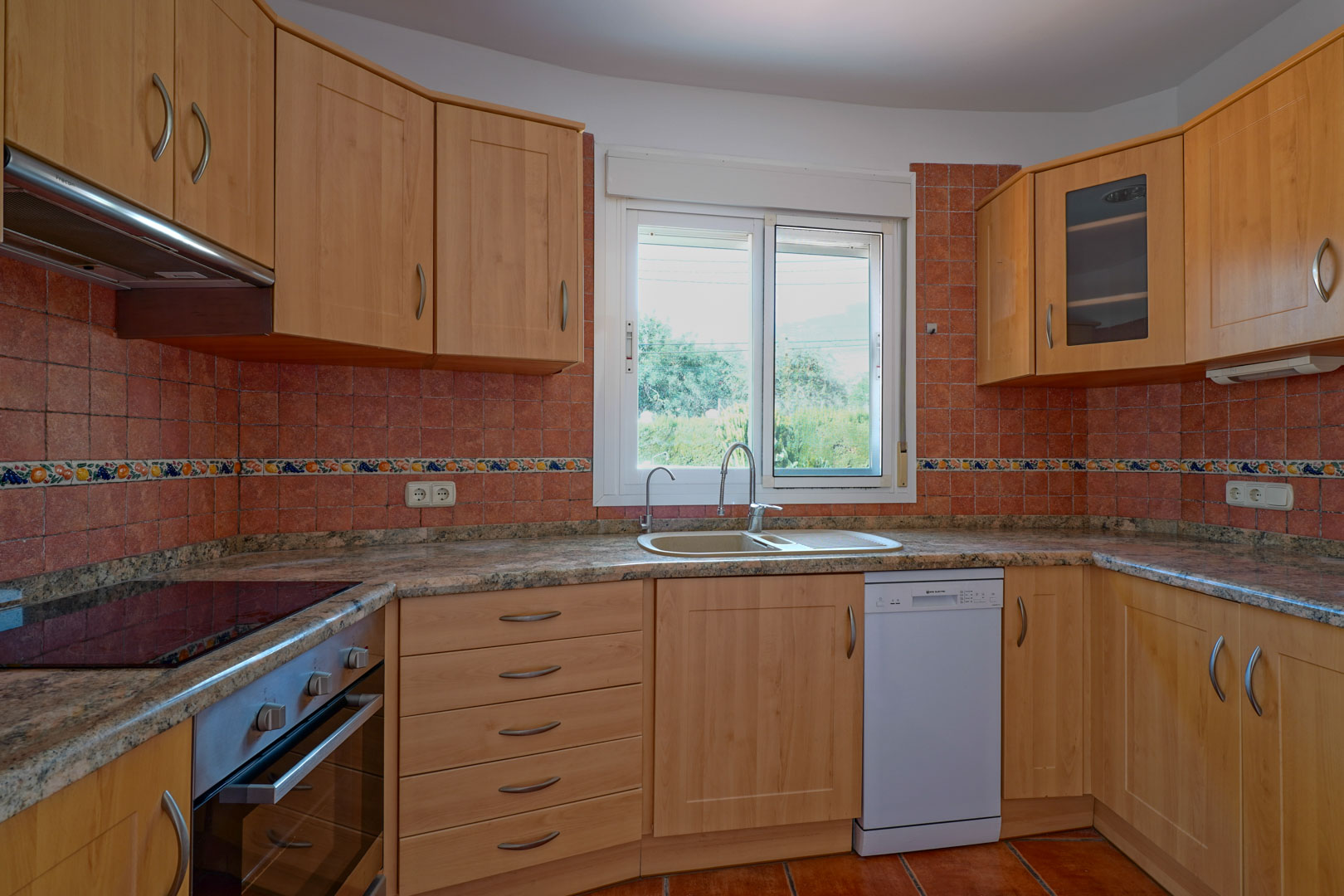 Independent kitchen featuring wood cabinetry, granite countertops, and a rustic tiled backsplash. It includes a built-in oven, dishwasher, and a window for natural light.