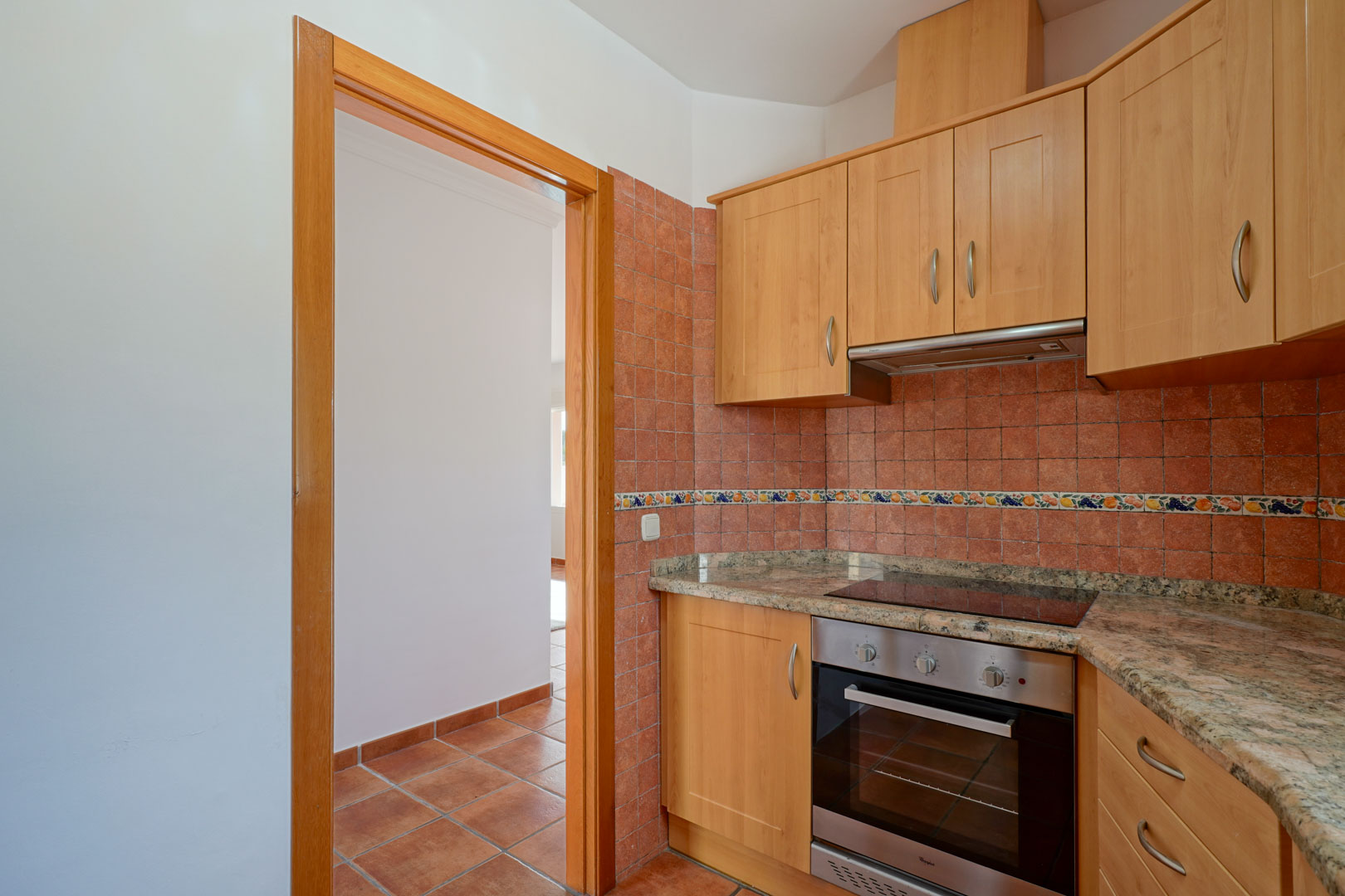 Independent kitchen featuring wood cabinetry, granite countertops, and integrated appliances. The space includes rustic wall tiling and traditional terracotta floor tiles.