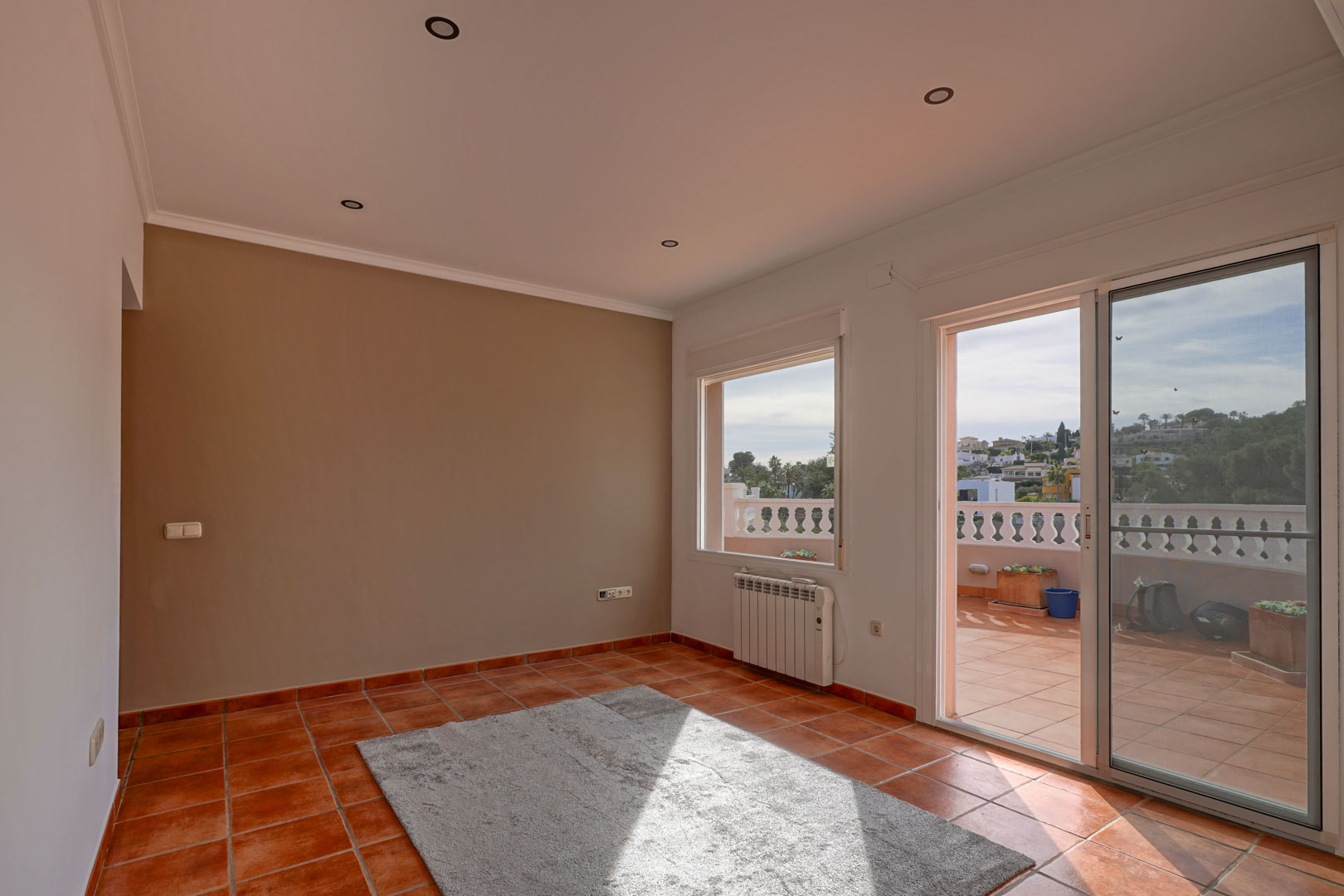 Living area featuring terracotta tile flooring, recessed lighting, and a sliding glass door opening onto a spacious terrace with a classic balustrade.
