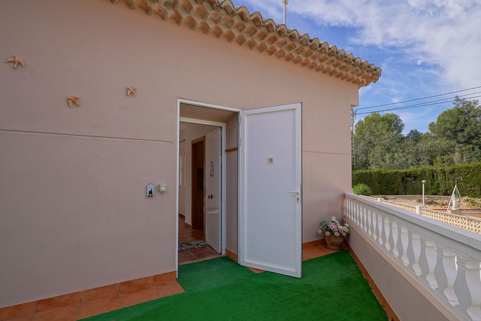 Main entrance to the penthouse from the upper terrace, featuring a white door, terracotta flooring, and a classic balustrade overlooking the greenery.