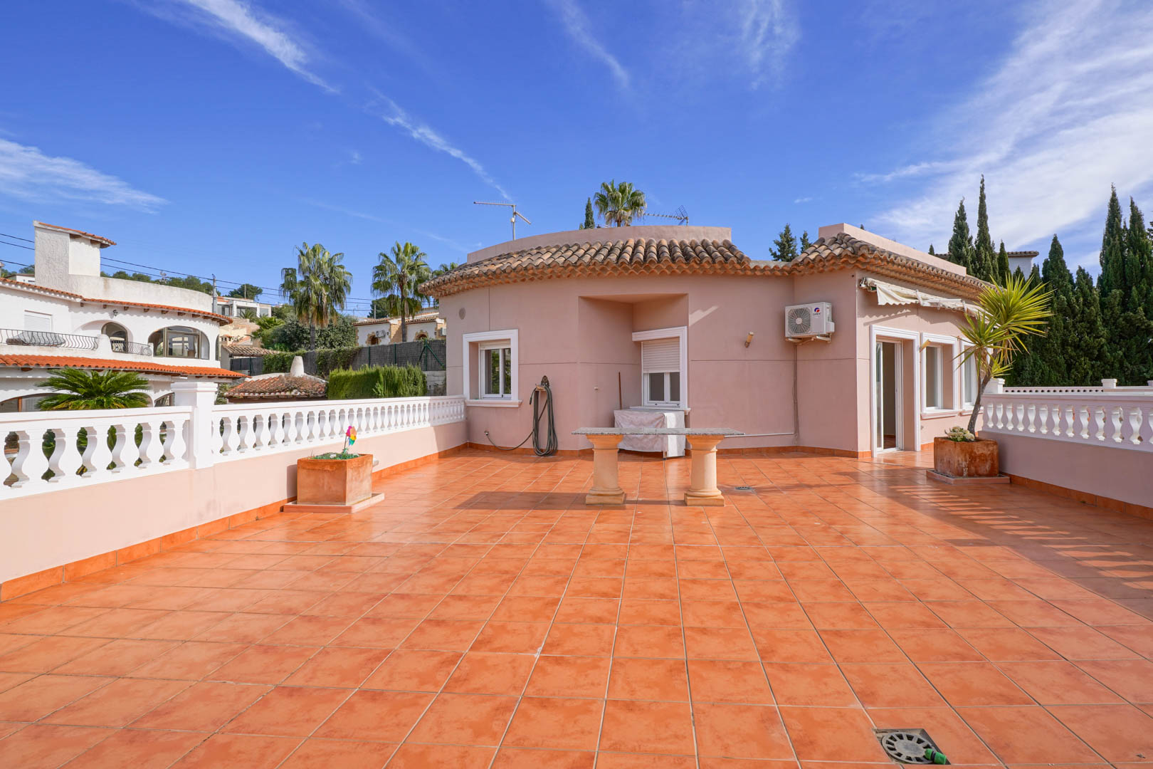 Spacious rooftop terrace featuring terracotta tiling, a white balustrade, and a stone table, set against a backdrop of Mediterranean architecture.