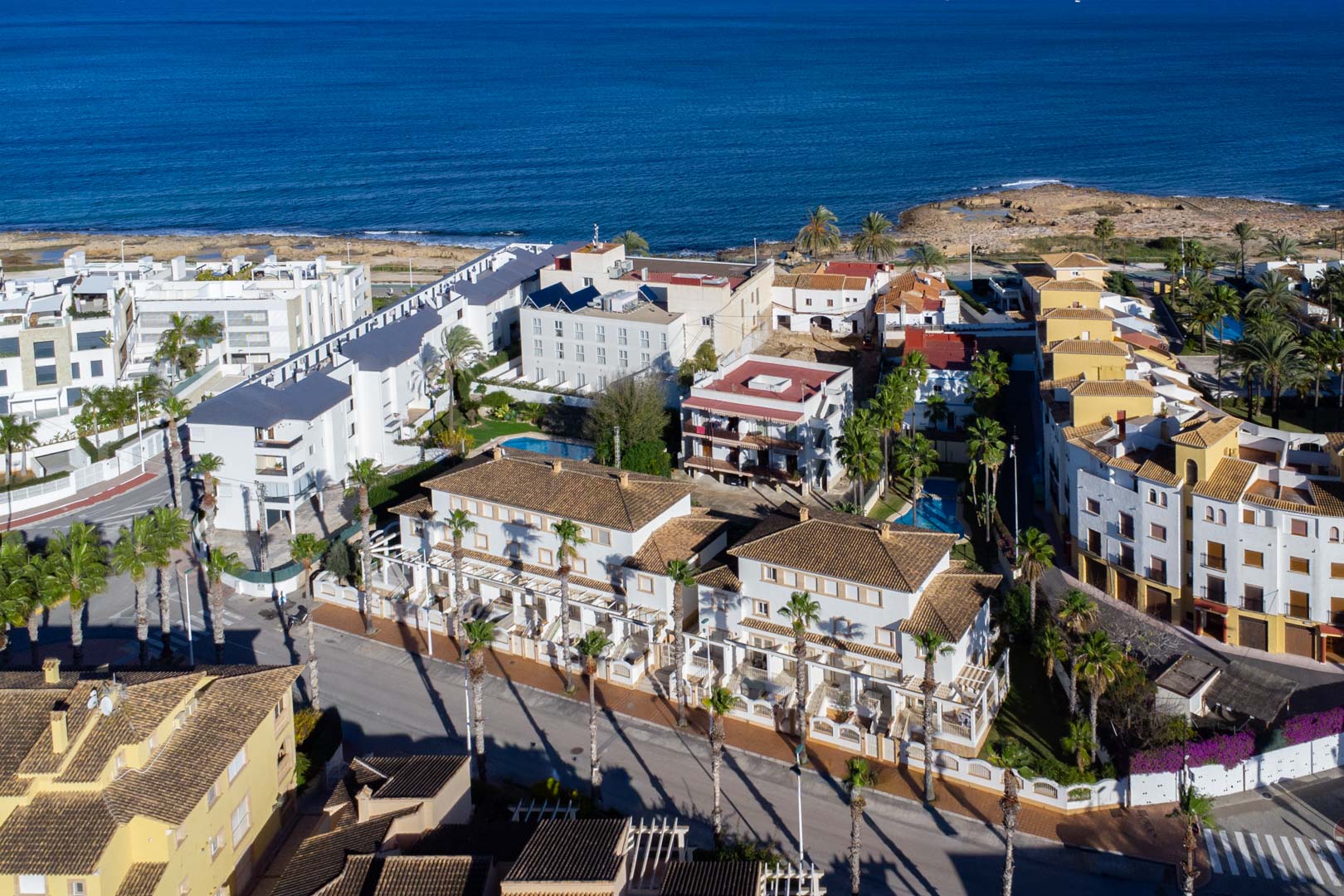Aerial view of the Calle Génova complex, highlighting its proximity to the Mediterranean Sea and the white facades with terracotta roofs lined with palm trees.
