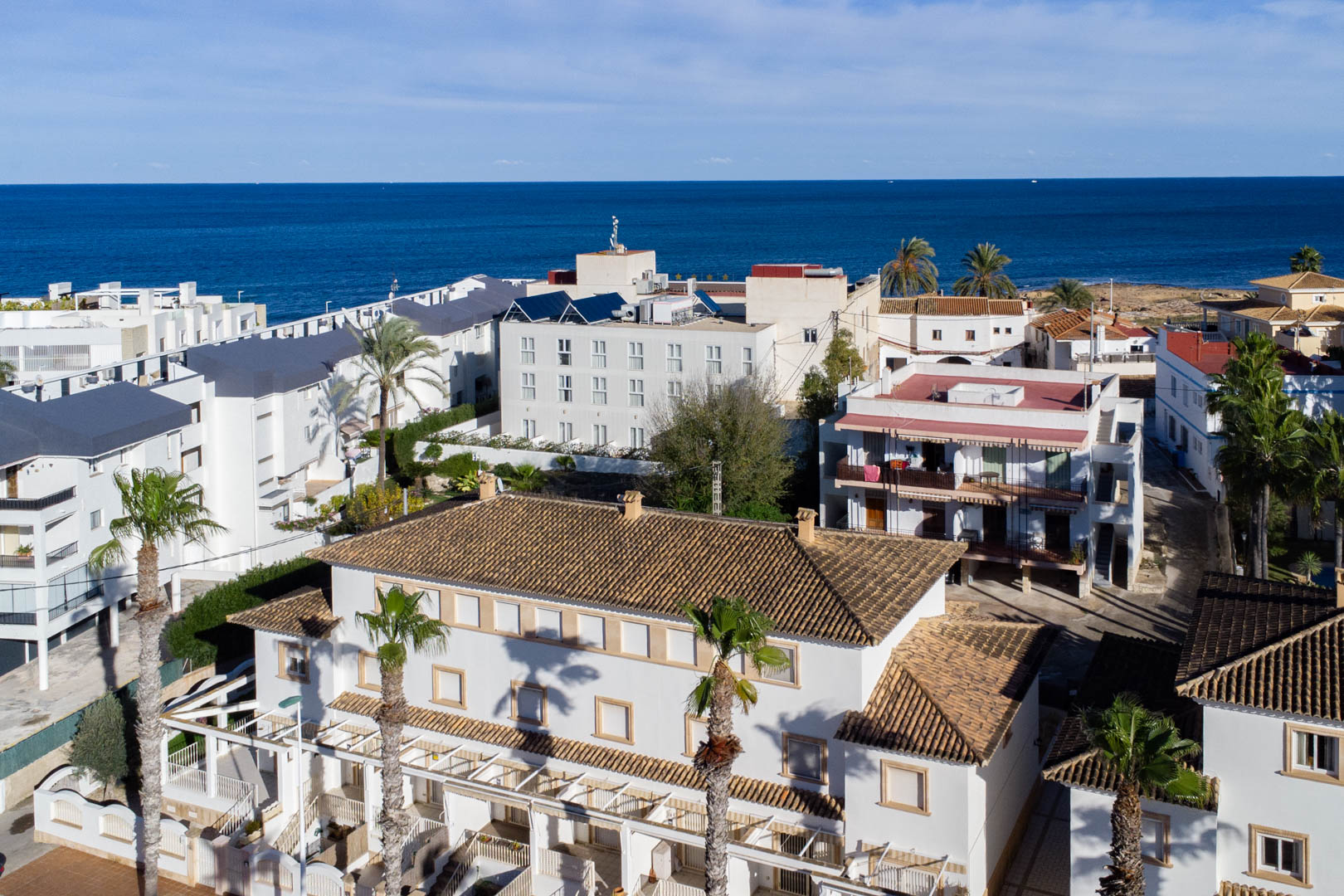 Aerial view of the residential complex featuring white facades, terracotta tiled roofs, and private terraces, set against the backdrop of the Mediterranean Sea.