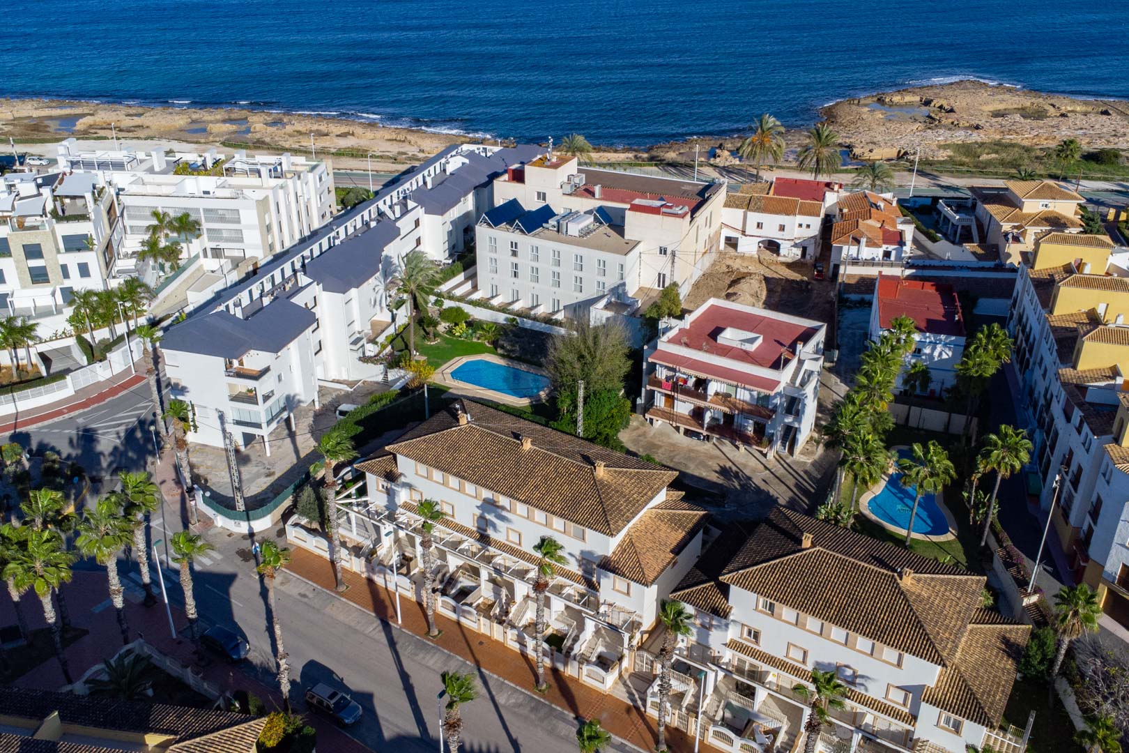Aerial view of the residential complex on Calle Génova, showing its proximity to the Mediterranean Sea, communal pools, and traditional tiled roofs.