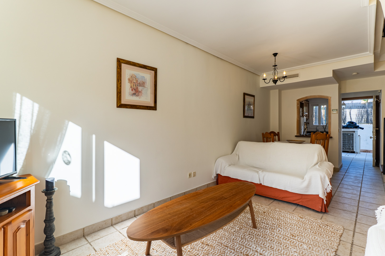 Bright living area featuring ceramic tile flooring, a wooden coffee table, and a functional pass-through to the kitchen with views toward the rear patio.