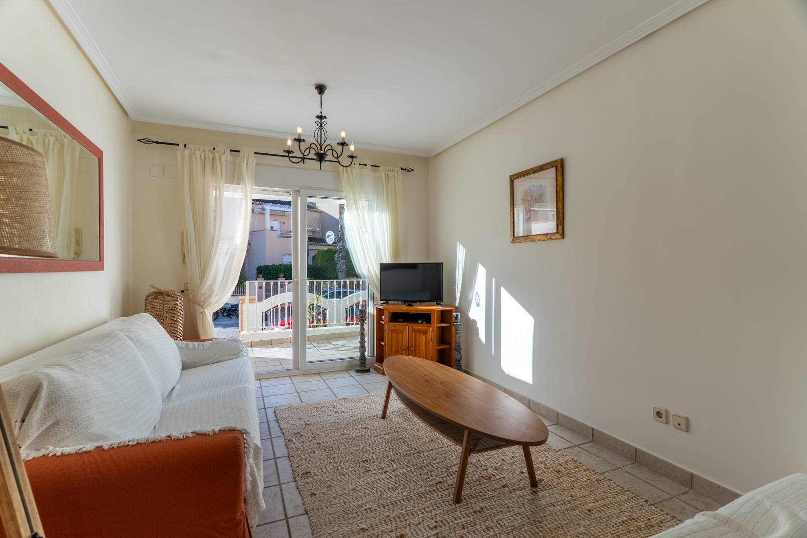 Bright living area featuring tiled flooring, an oval wooden coffee table, and direct access to a private terrace through sliding glass doors.