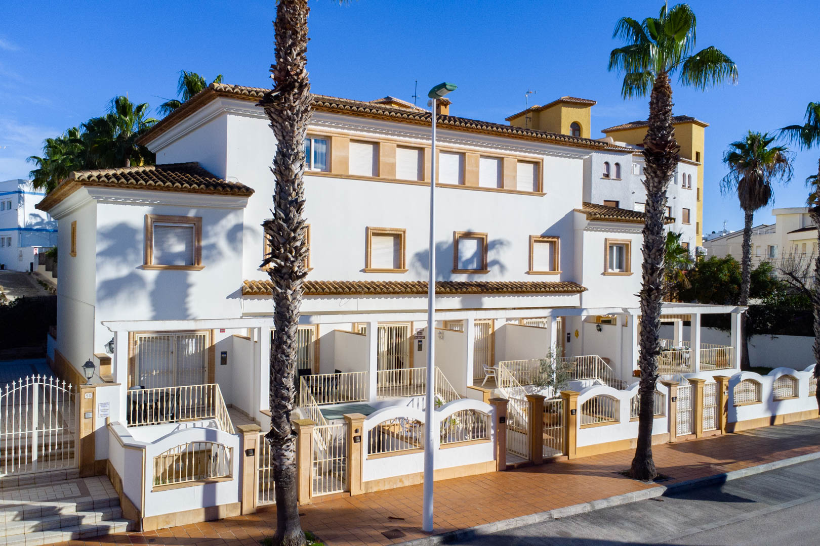 Exterior facade of Mediterranean-style triplex townhouses featuring white walls, stone window trims, and private gated front terraces.
