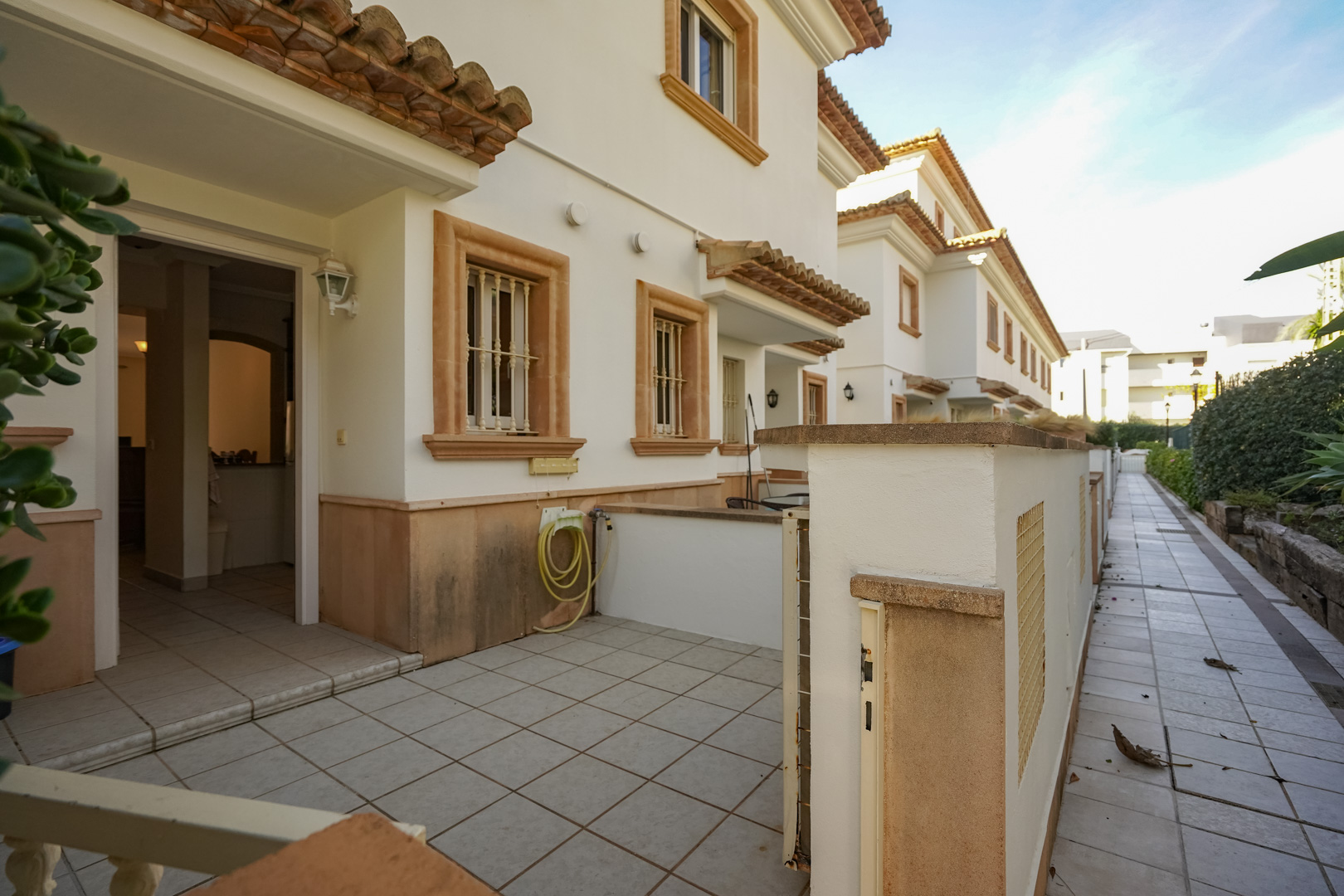 Exterior facade of the triplex featuring a tiled front terrace, Tosca stone window surrounds, and direct access from the urbanization's pedestrian walkway.