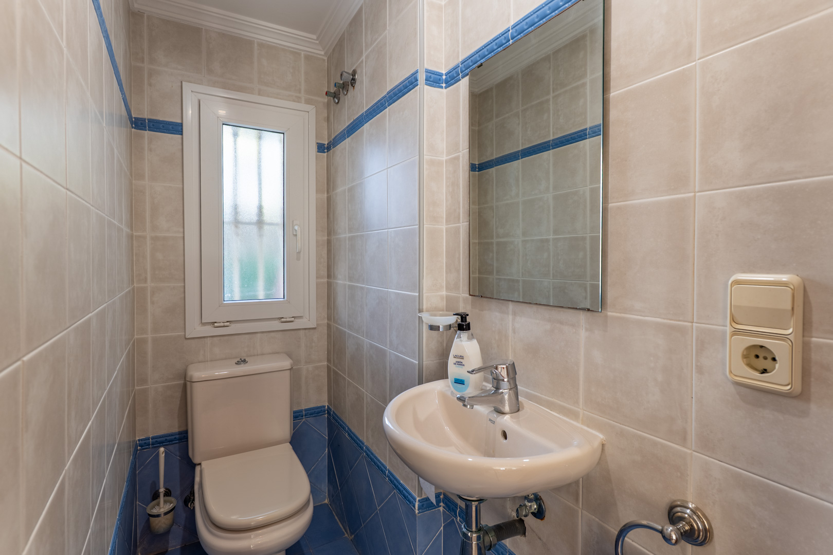 Guest toilet featuring beige and blue ceramic tiling, a white porcelain sink, and a frosted glass window for natural light and ventilation.