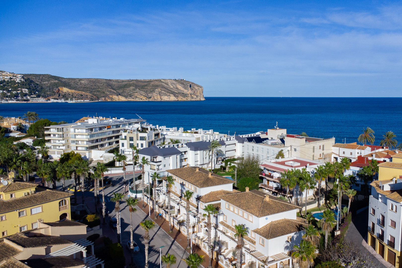 Panoramic aerial view of Jávea showcasing the proximity to the Mediterranean Sea and Cabo de San Antonio, featuring traditional tiled roofs and palm-lined streets.