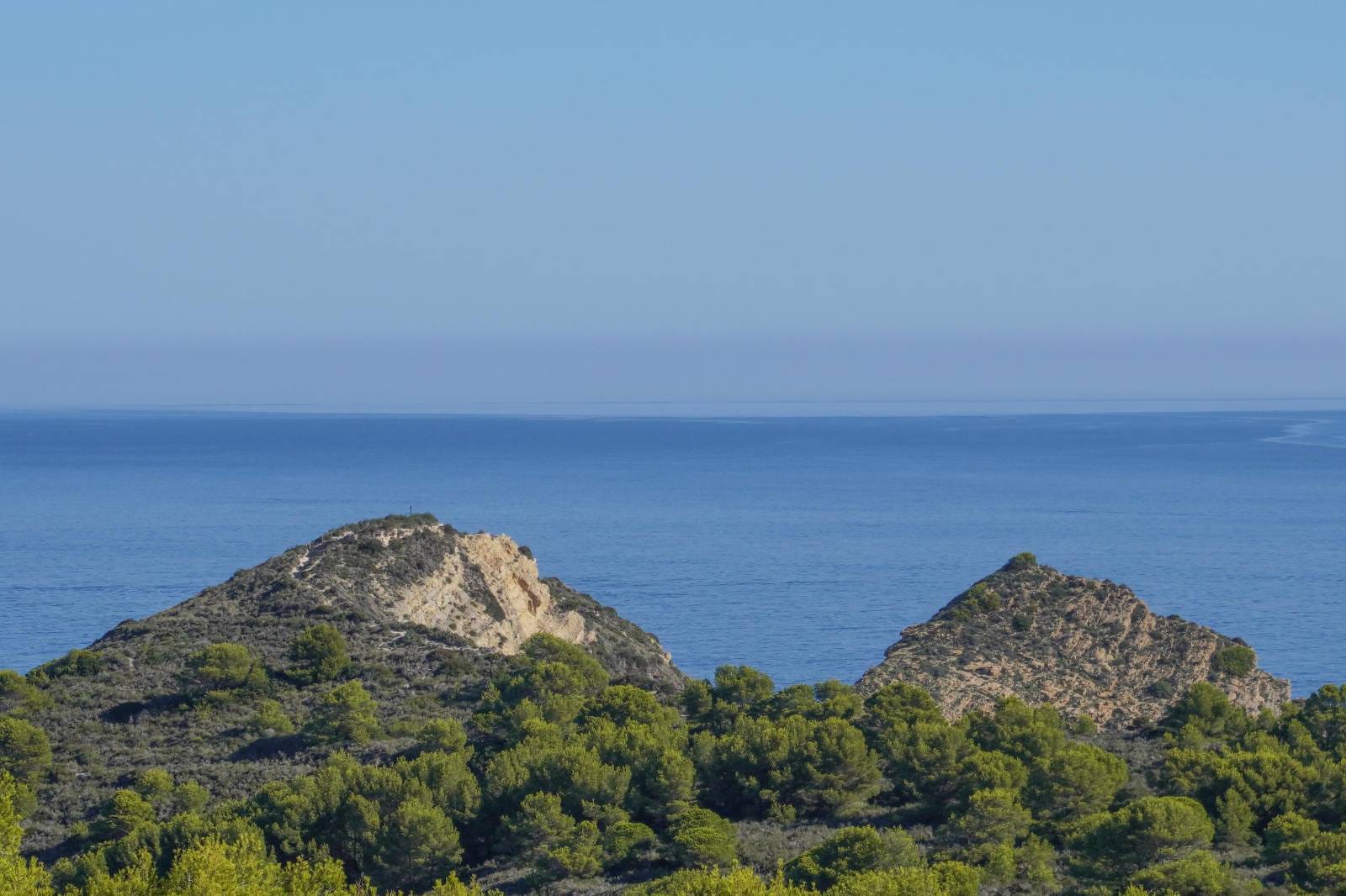 Panoramic Mediterranean Sea views featuring rugged coastal hills and lush pine forests under a clear blue horizon, visible from the upper levels.