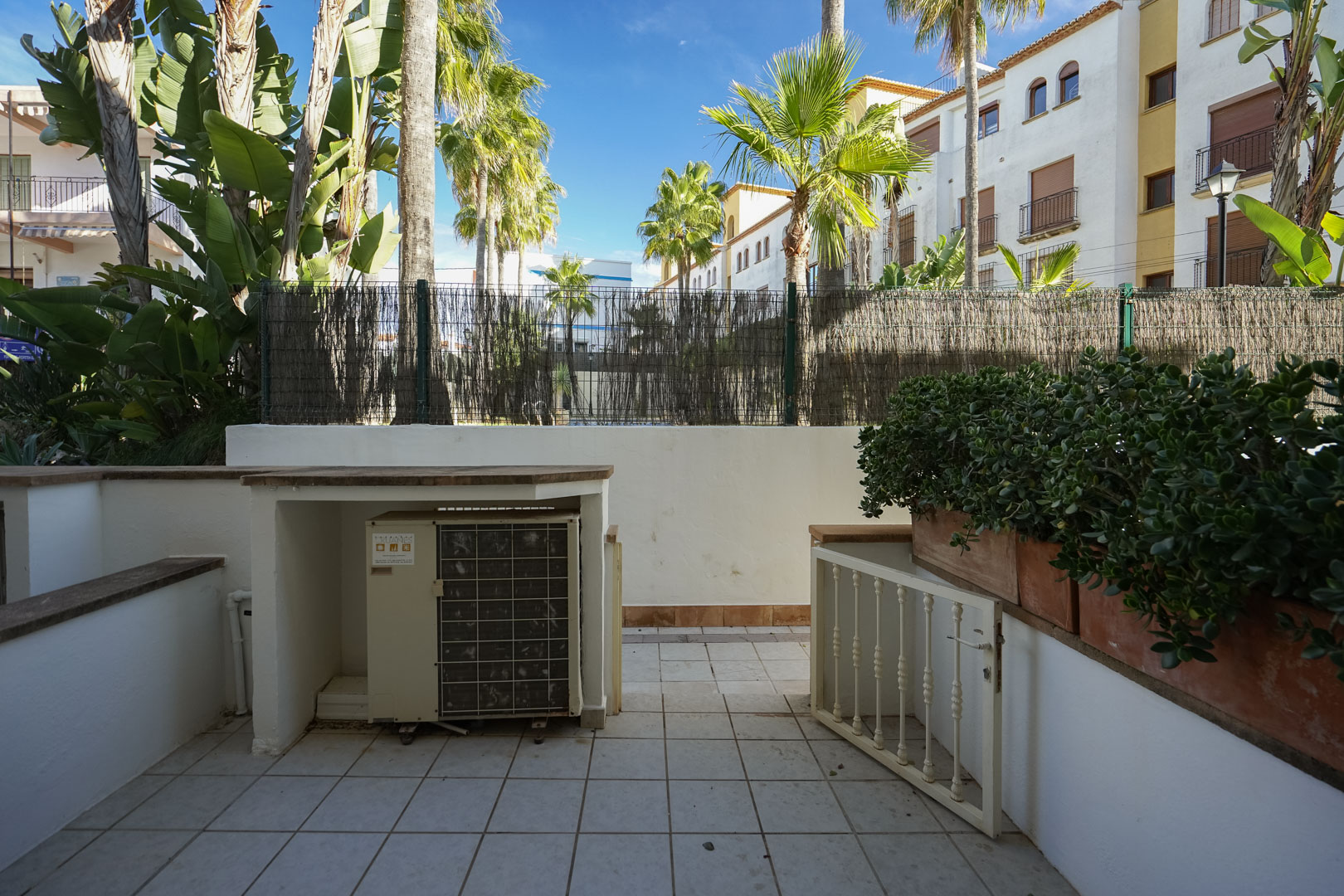 Private tiled terrace featuring a built-in air conditioning enclosure, integrated planters, and views of surrounding palm trees and Mediterranean greenery.
