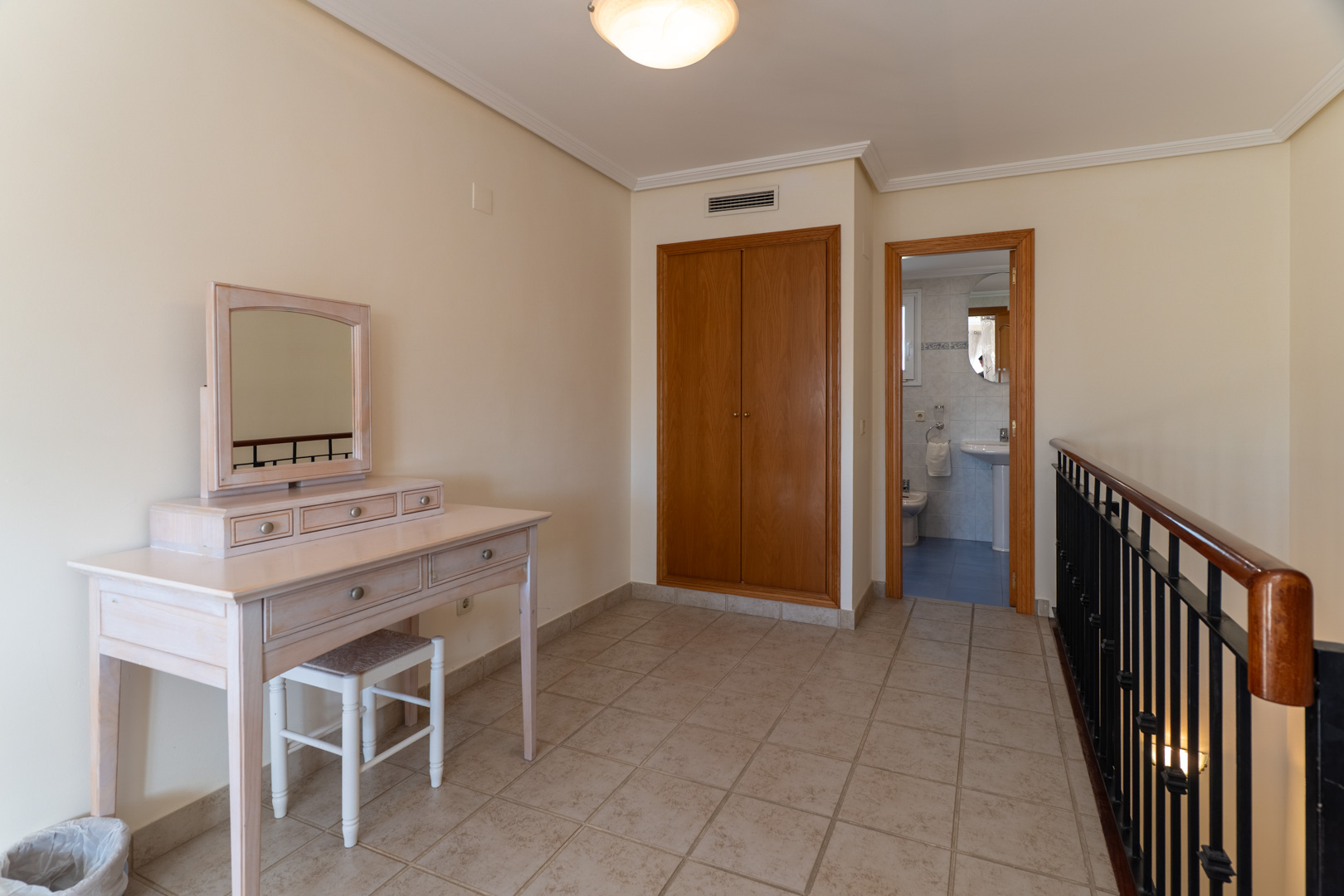 Upper floor landing featuring a light wood dressing table, built-in wardrobe, and access to an en-suite bathroom with blue tiling.