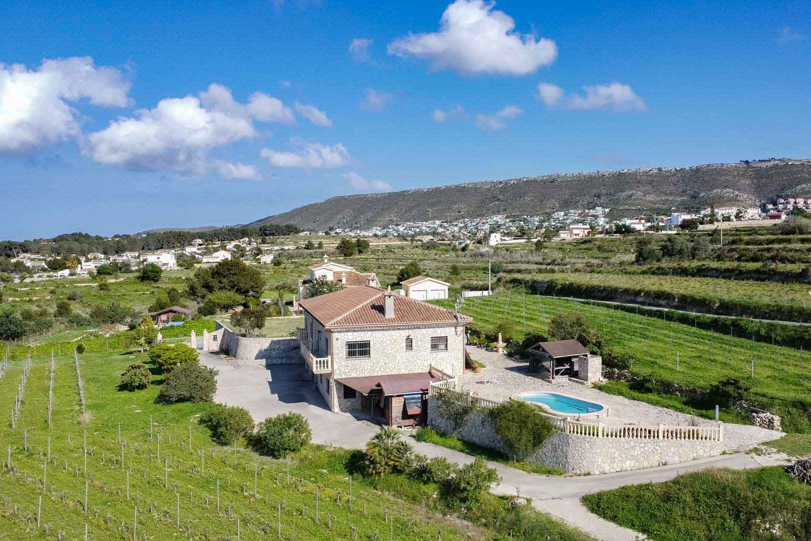 Aerial perspective of a stone-clad country villa featuring a private pool, sun terrace with stone balustrades, and expansive vineyards set against a mountain backdrop.
