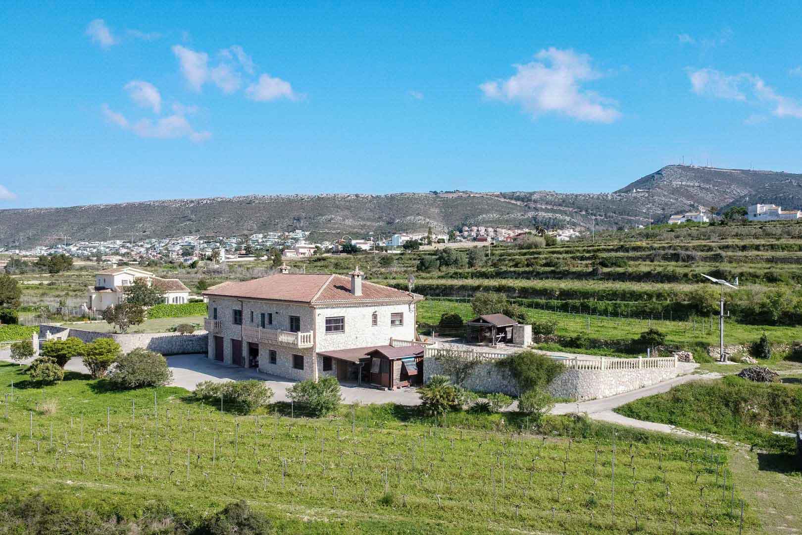 Aerial perspective of a two-story stone country house with terracotta roofing, nestled among private vineyards and terraced fields with mountain views.