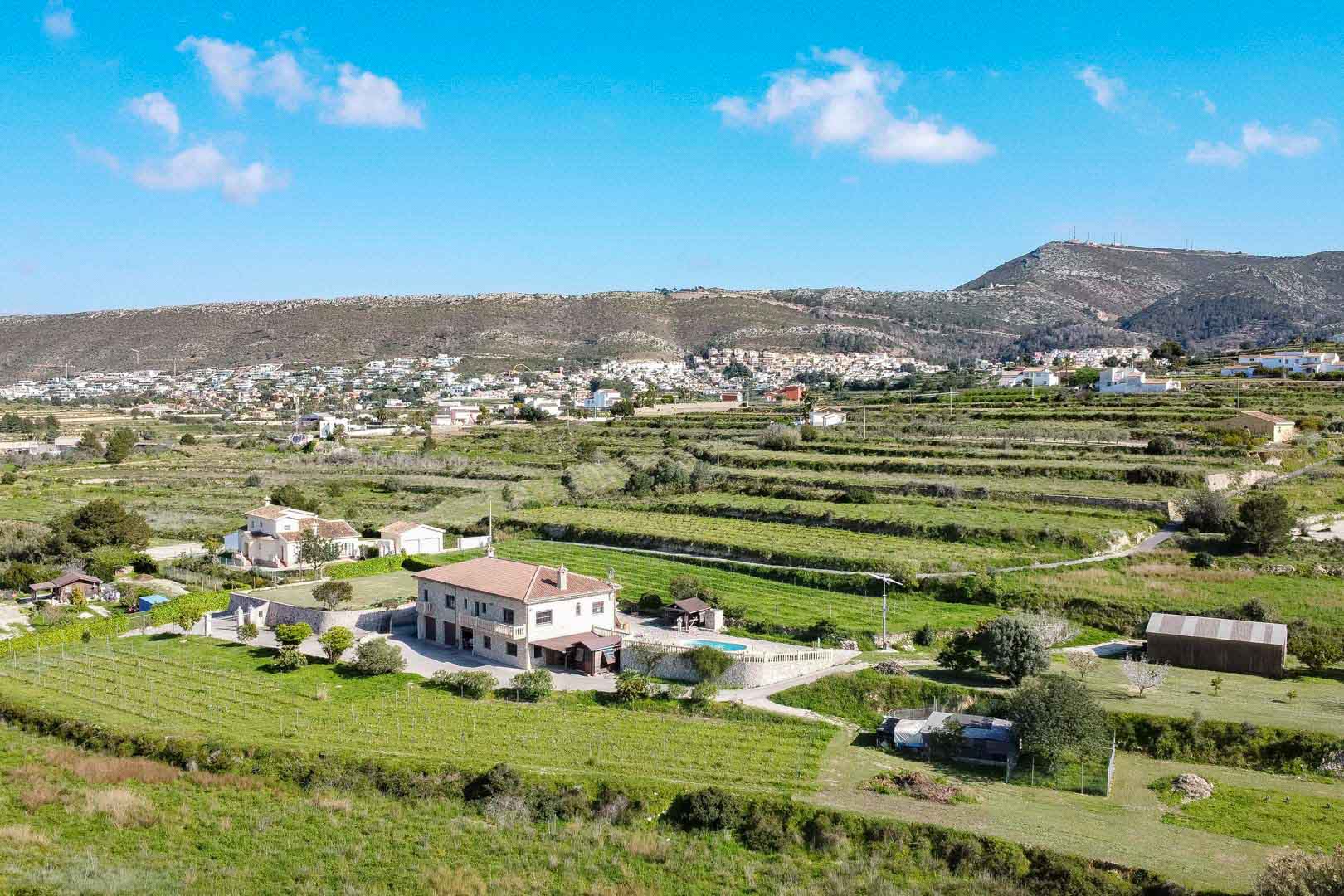 Aerial view of a two-story stone residence featuring a swimming pool and terraced agricultural land against a mountain backdrop.