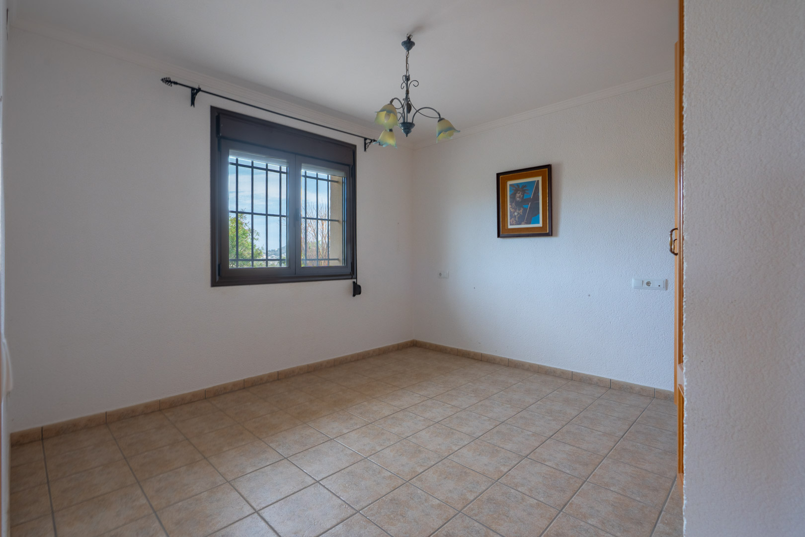 Empty interior room featuring ceramic tile flooring, textured white walls, and a window with security bars and a dark frame.
