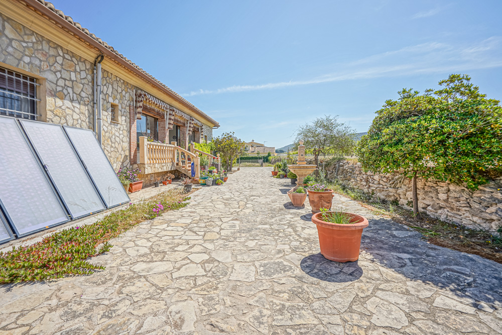 Exterior stone patio with flagstone paving, featuring a stone fountain, terracotta planters, and solar thermal panels against the masonry wall.