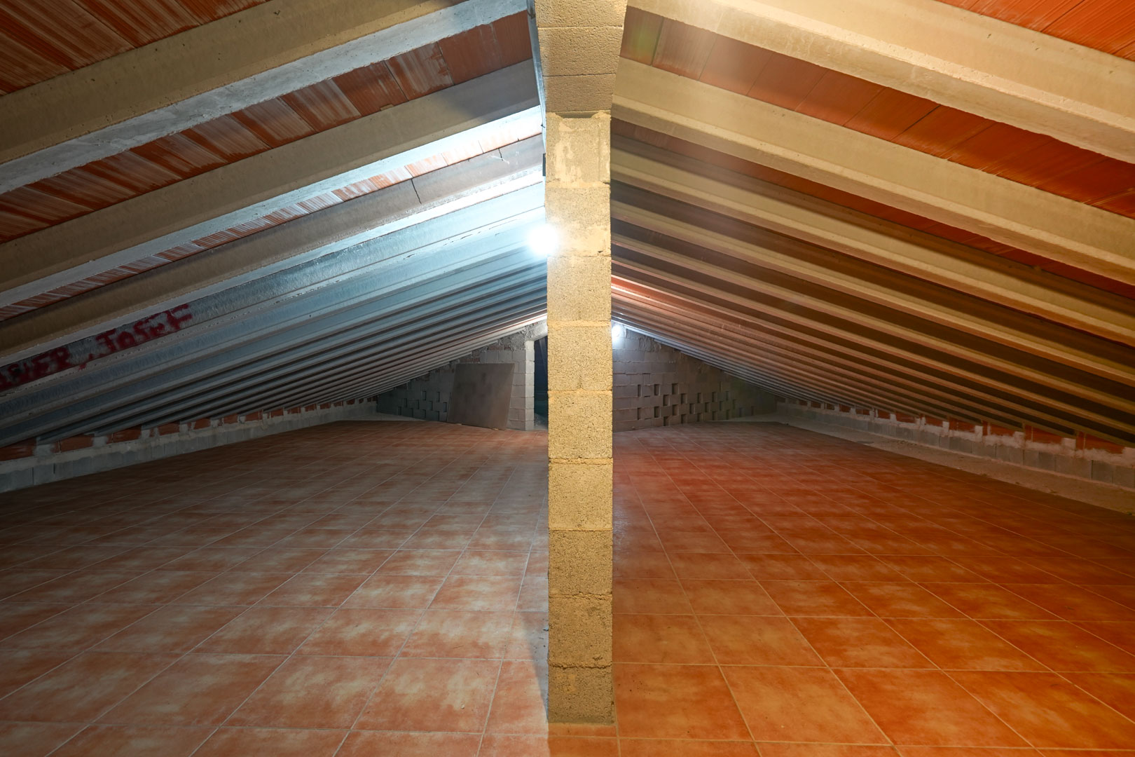 Spacious attic storage area featuring a sloped ceiling with exposed concrete beams, terracotta tiles, and a central support pillar.