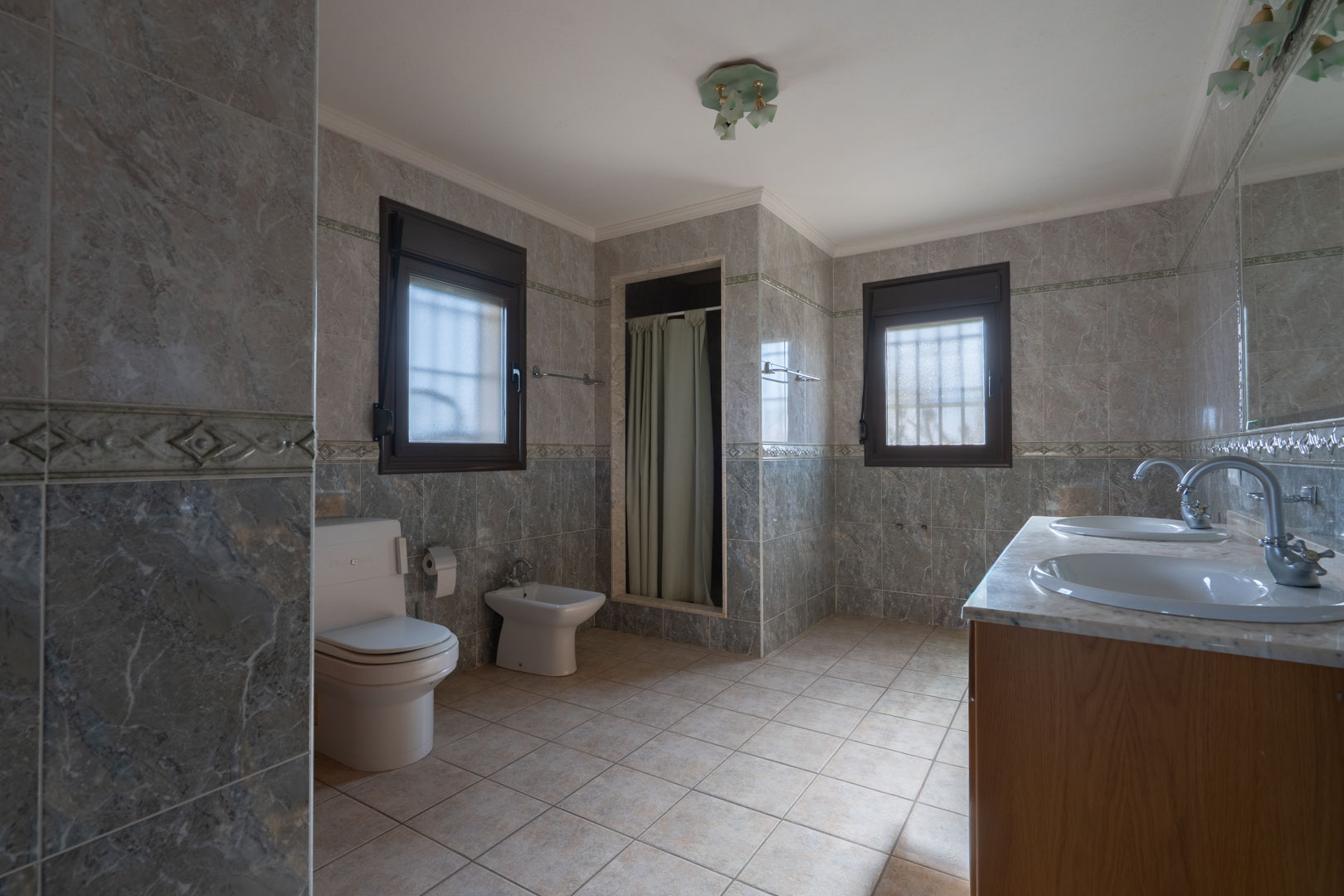 Spacious bathroom featuring a double marble vanity, grey marble-effect wall tiling with decorative borders, and two frosted glass windows.