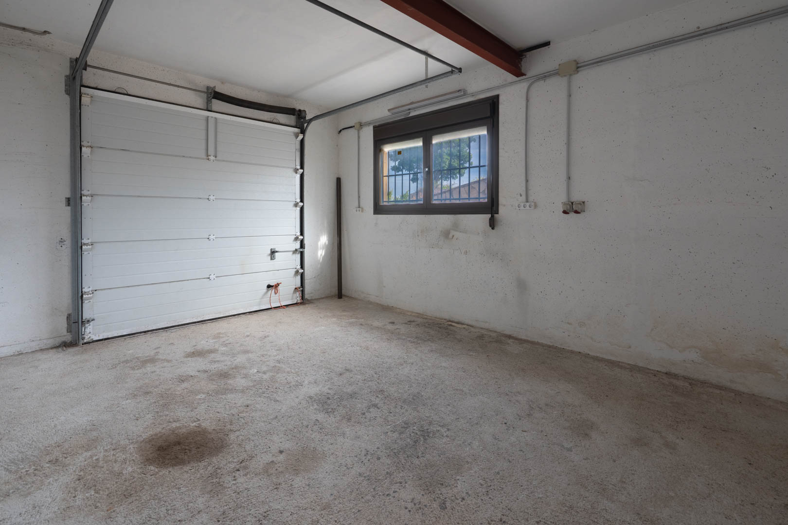 Spacious garage featuring a concrete floor, white sectional overhead door, and a window with security bars providing natural light.