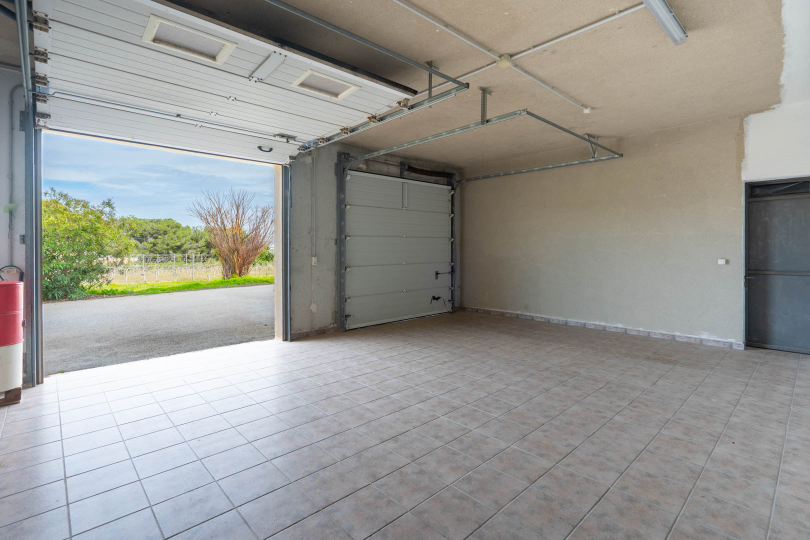 Spacious garage with ceramic tile flooring, featuring two sectional doors and fluorescent lighting. Provides direct access to the paved driveway and garden.