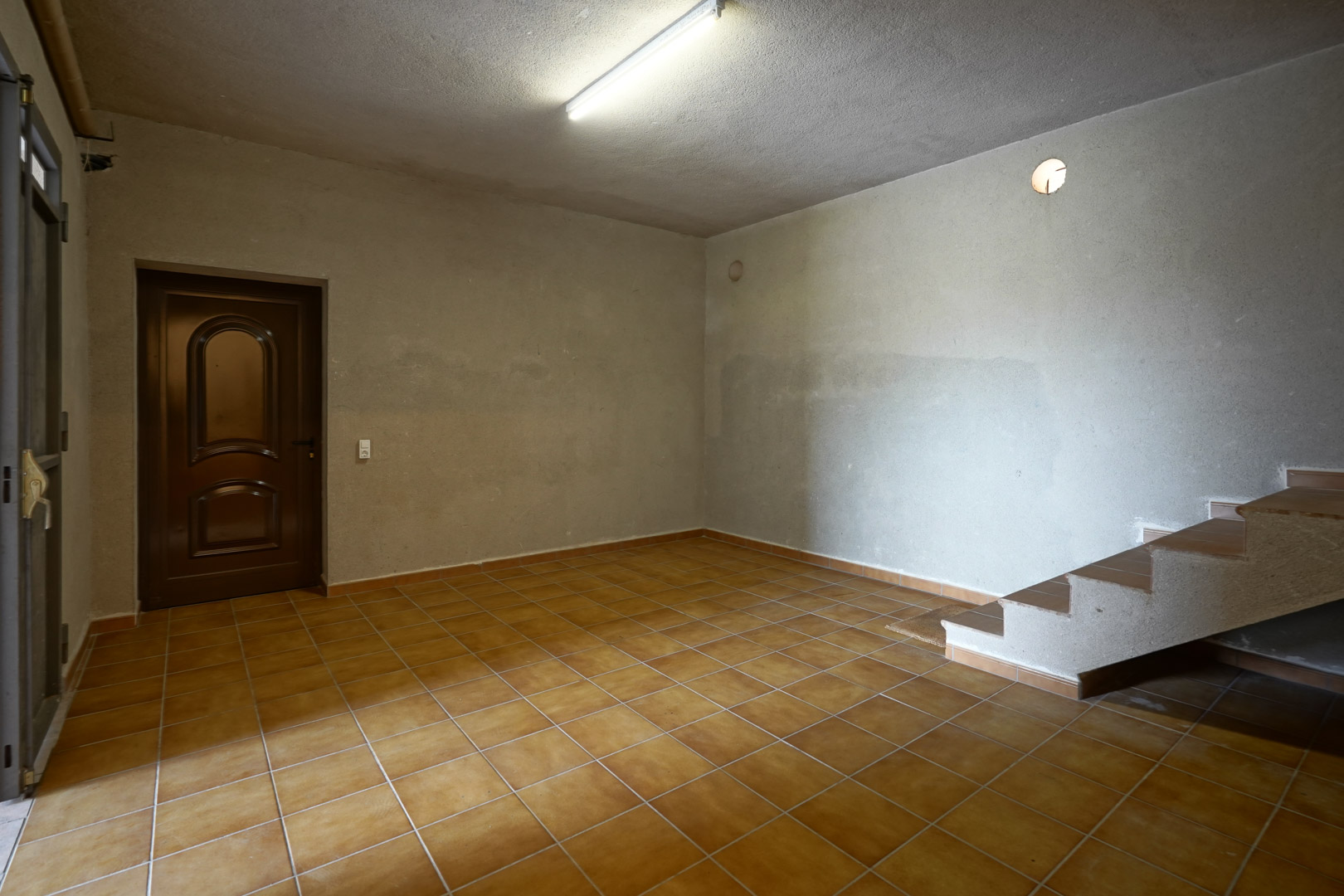 Spacious utility room featuring terracotta tile flooring, textured plaster walls, and a tiled staircase leading to the upper level.