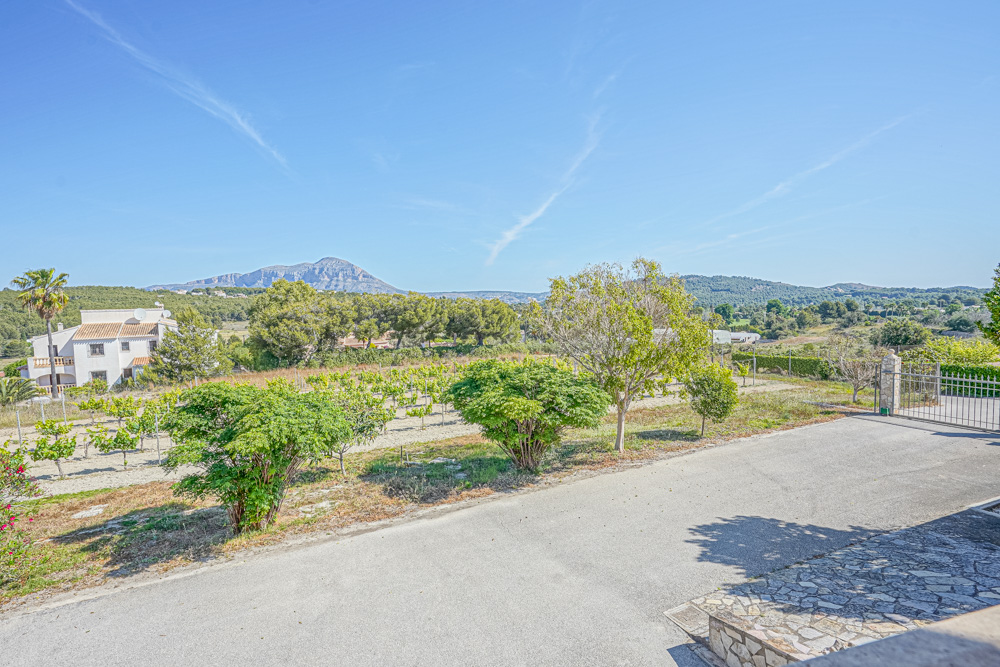 View from the paved driveway overlooking a private vineyard and Mediterranean landscape with the Montgó mountain in the background.
