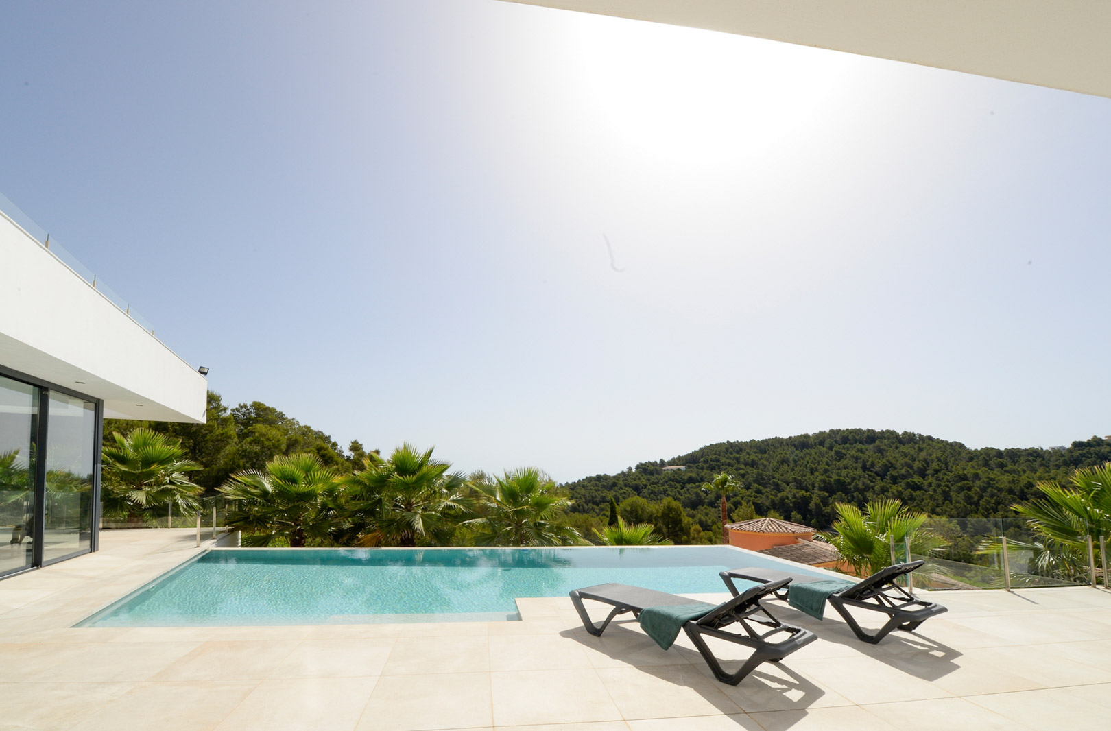 Infinity pool and sun terrace with black loungers, offering panoramic views of the Mediterranean hills and surrounding pine forests.