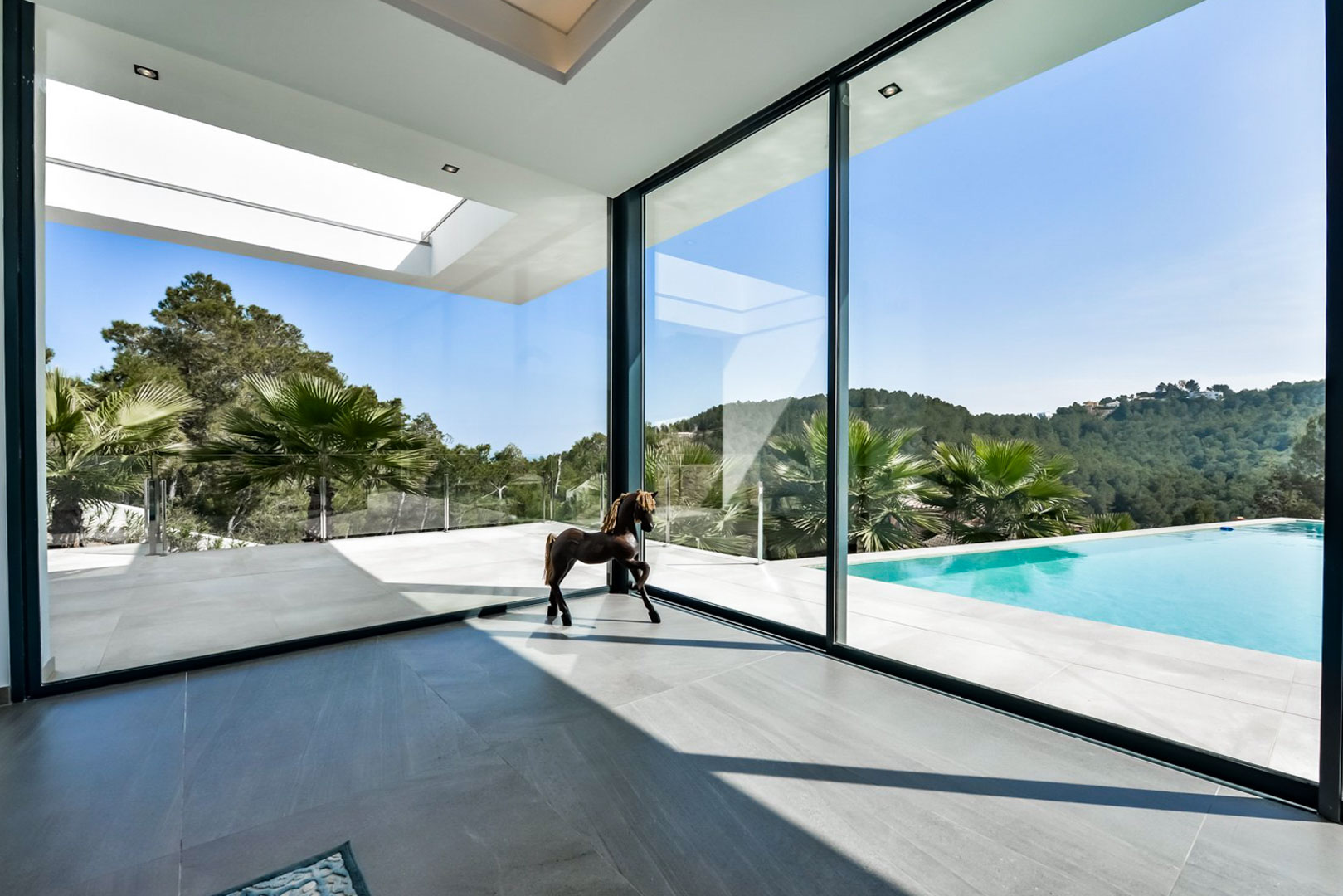 Living area featuring floor-to-ceiling glass walls that open onto a sun terrace with an infinity pool and views of the Mediterranean landscape.