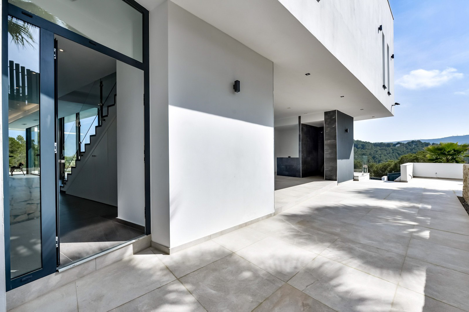 Main entrance and covered terrace featuring minimalist white architecture, porcelain flooring, and panoramic views of the surrounding green hills.